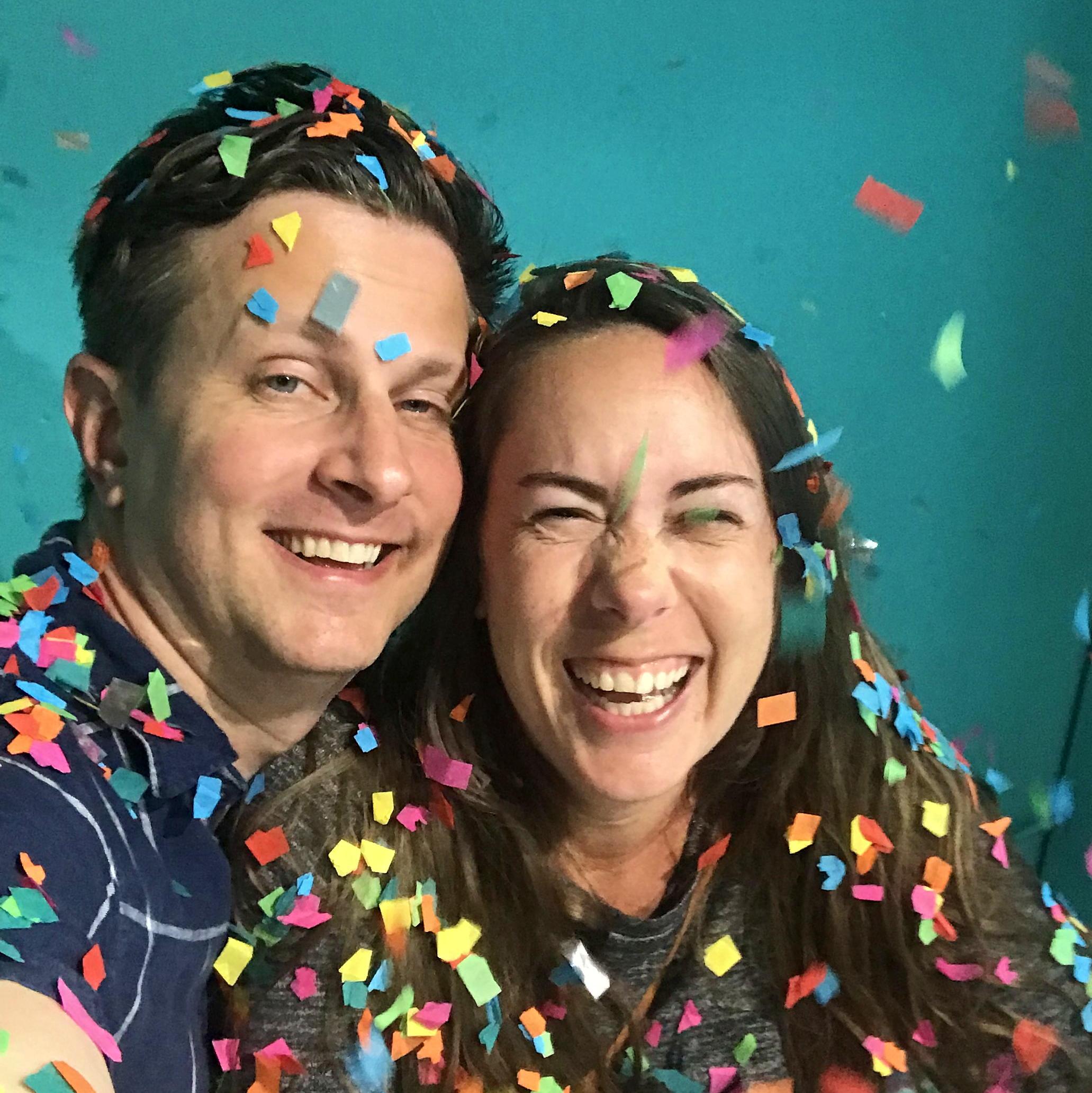 Ruth and James smile as multicolored confetti rains down on them.