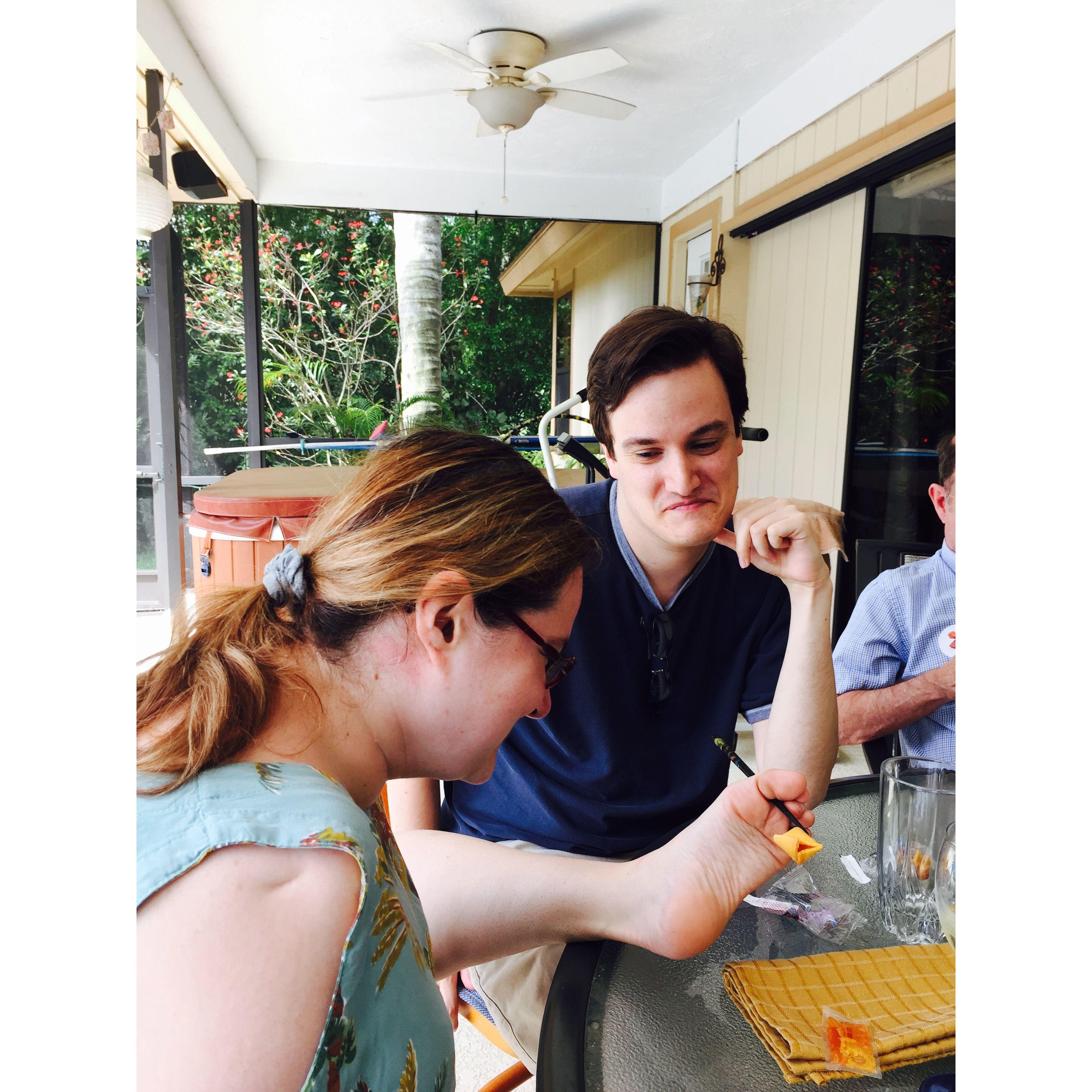 Olivia and zac sitting on a patio table eating. Zac looks at Olivia lovingly.