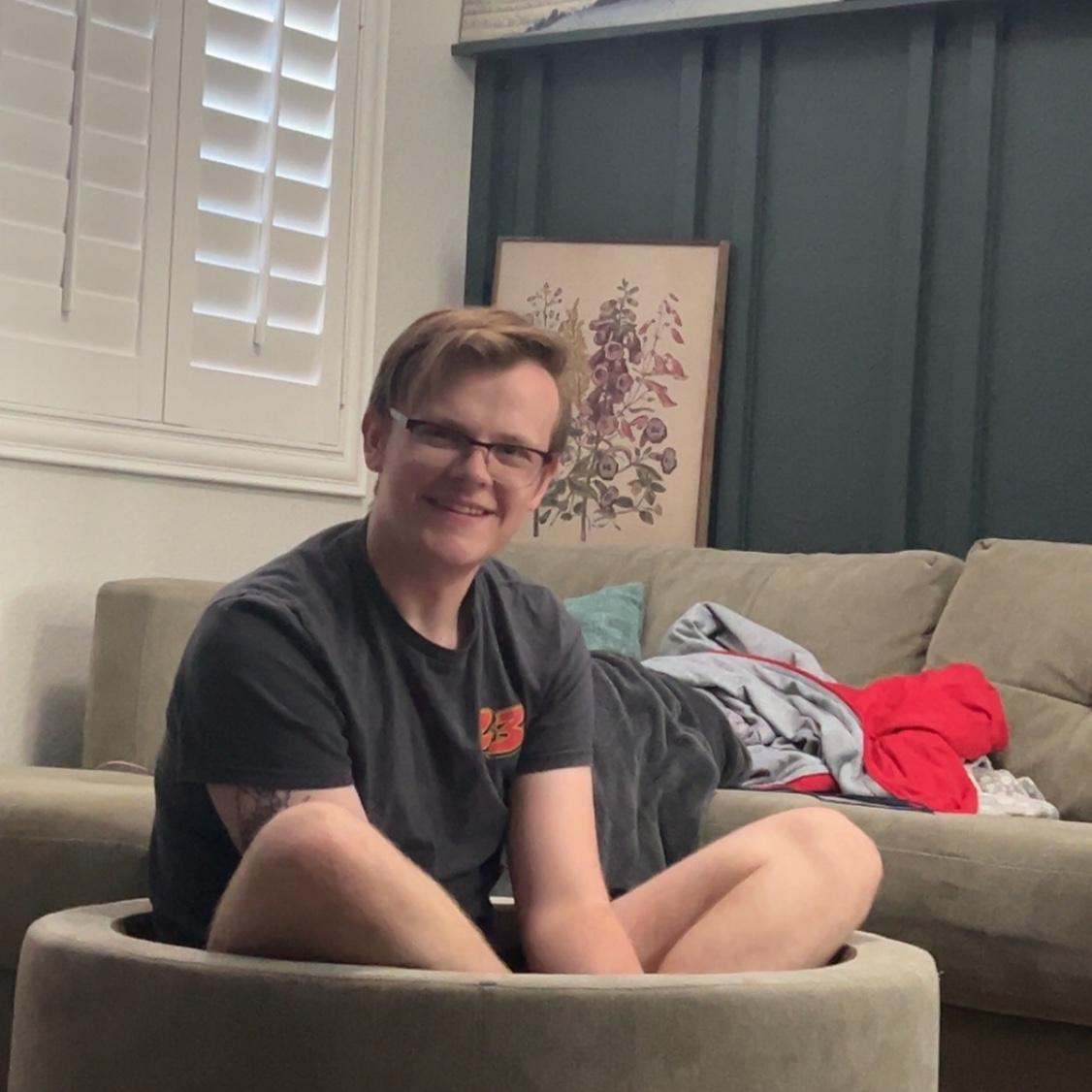 Zach being goofy, sitting inside the couch’s ottoman.