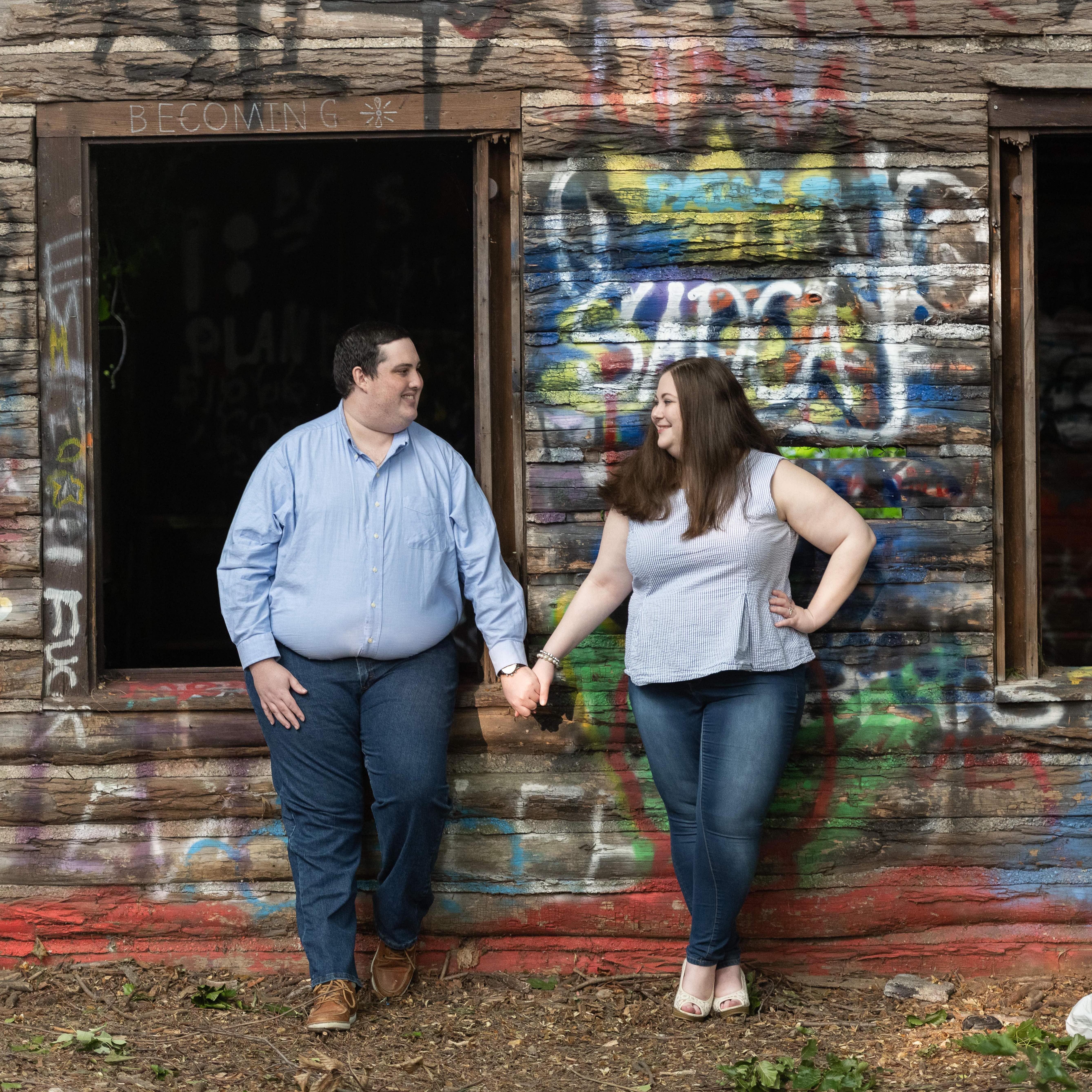 Marissa and Matt holding hands in front of a shack with colorful Graffiti on it