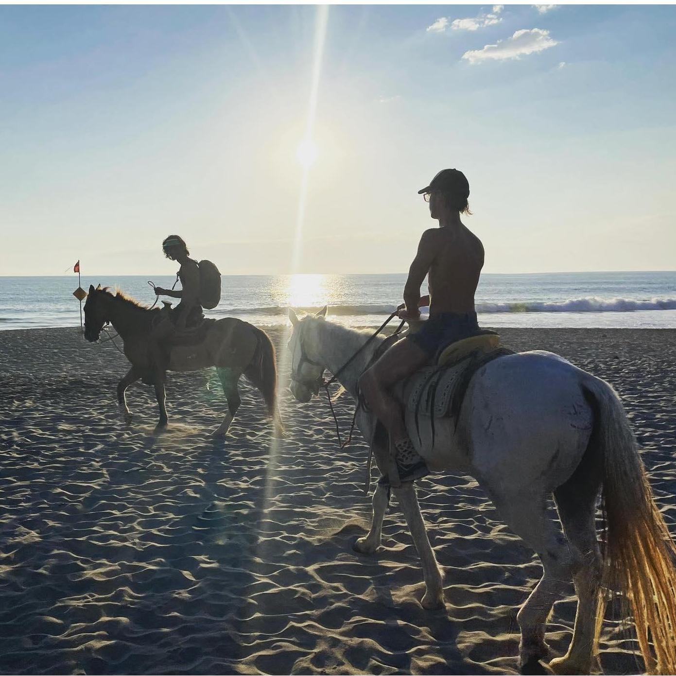 Zicatela Beach Puerto Escondido. Lane and John-Paul ride horses down a long empty beach as the sun sets on the water behind us