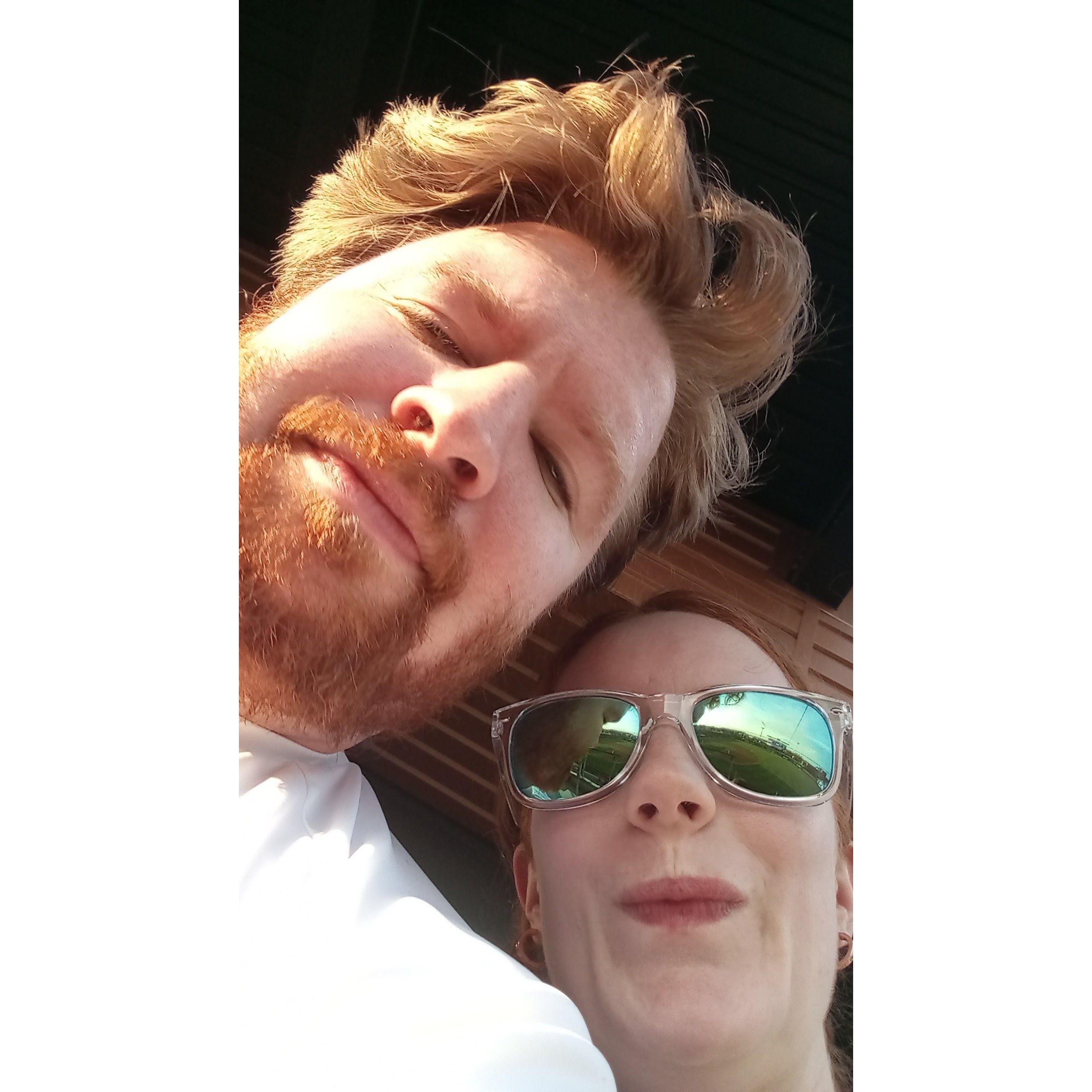 Amy & William snap a photo as the sun stares them directly in the face at a Wind Surge baseball game.