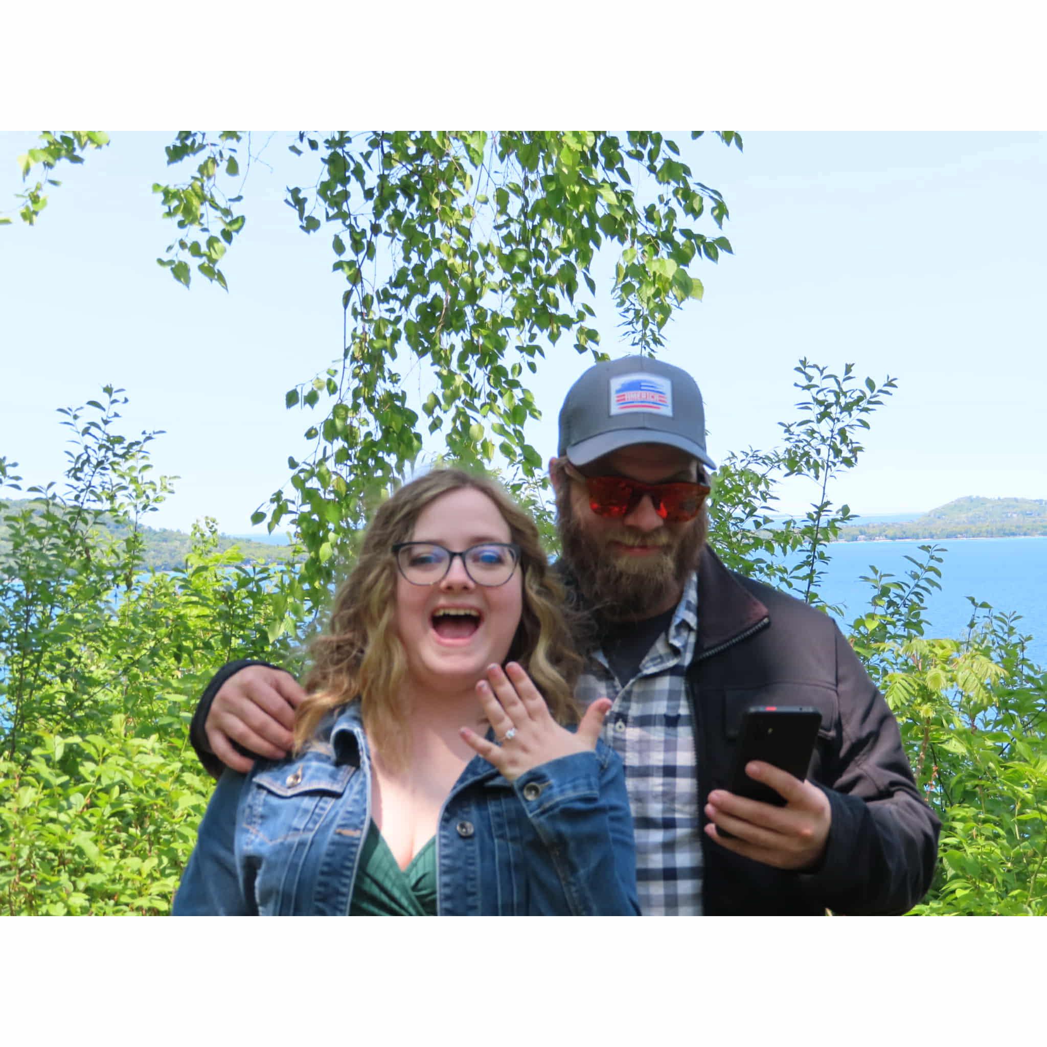 June 2025 - THE PROPOSAL! When they were in Leelanau for their annual trip, Devin said they were taking a scenic drive. The very first stop, he got his camera out to "take a picture" and proposed!