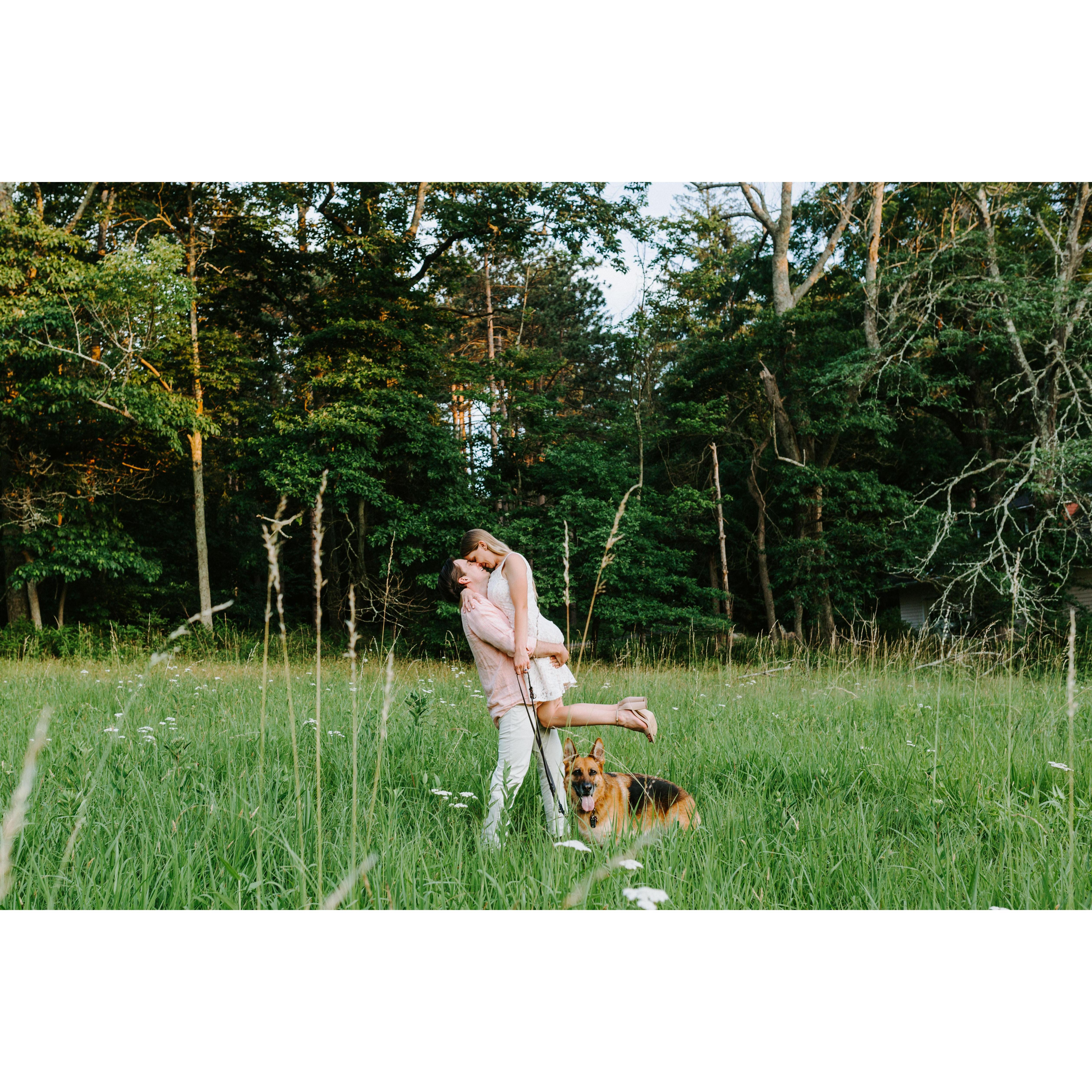 Matt holding my up by the waist so I am suspended in the. Foreheads touching. Halo stands watch and looks at the camera. We are in a green field surrounded by tall grass.