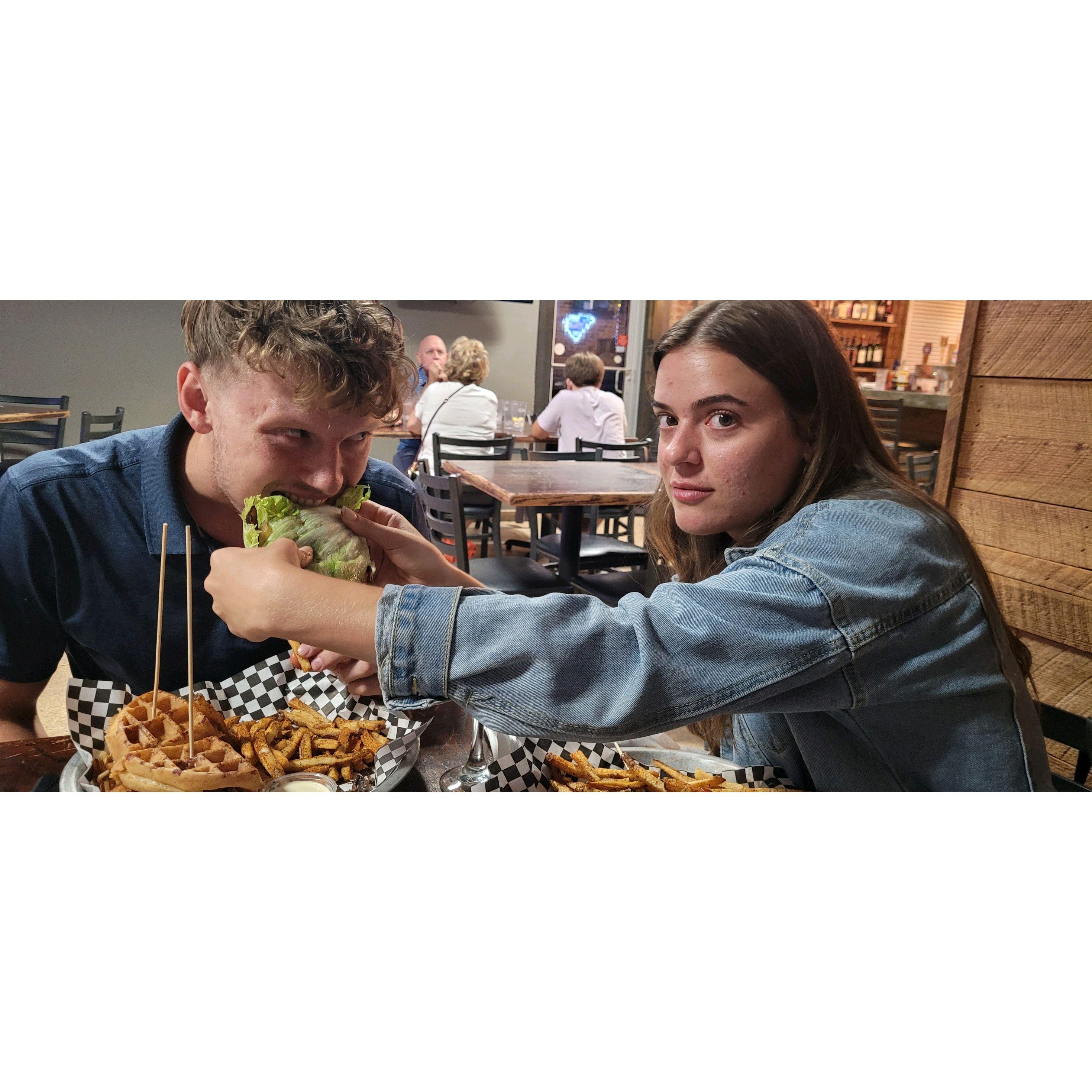Sharing more than just a meal – a moment of love and laughter as Olivia feeds Jonathan her protein-style burger