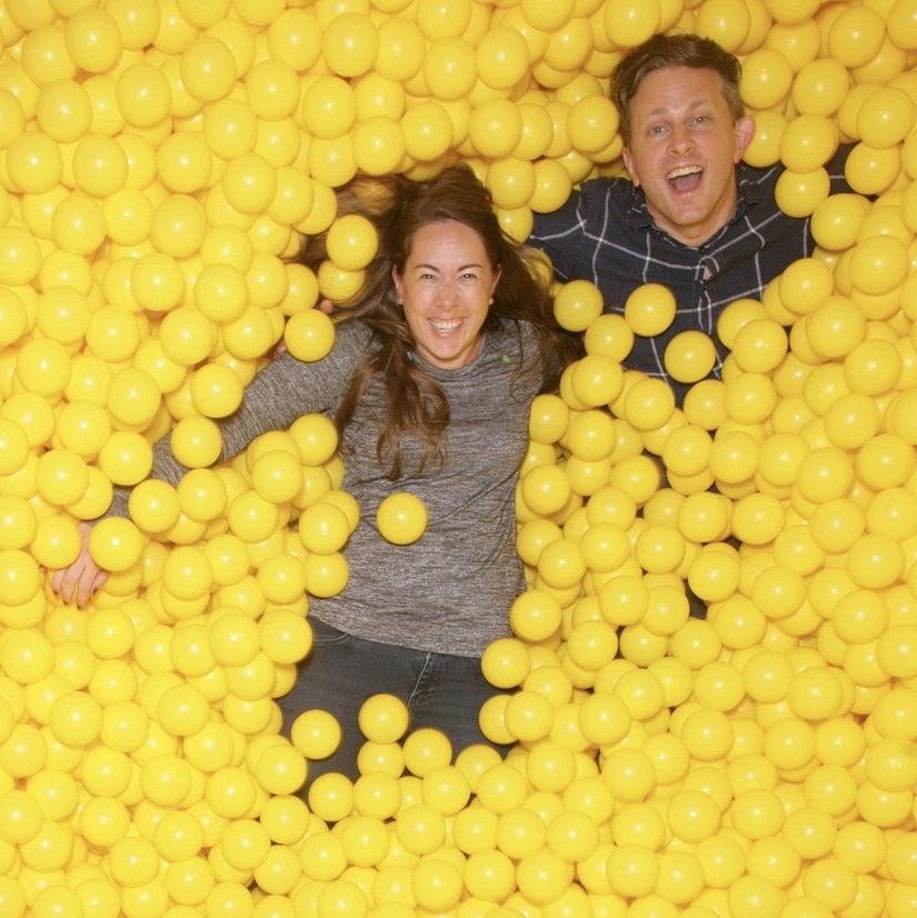 Ruth and James smiling while partly submerged in a pit of bright yellow balls.
