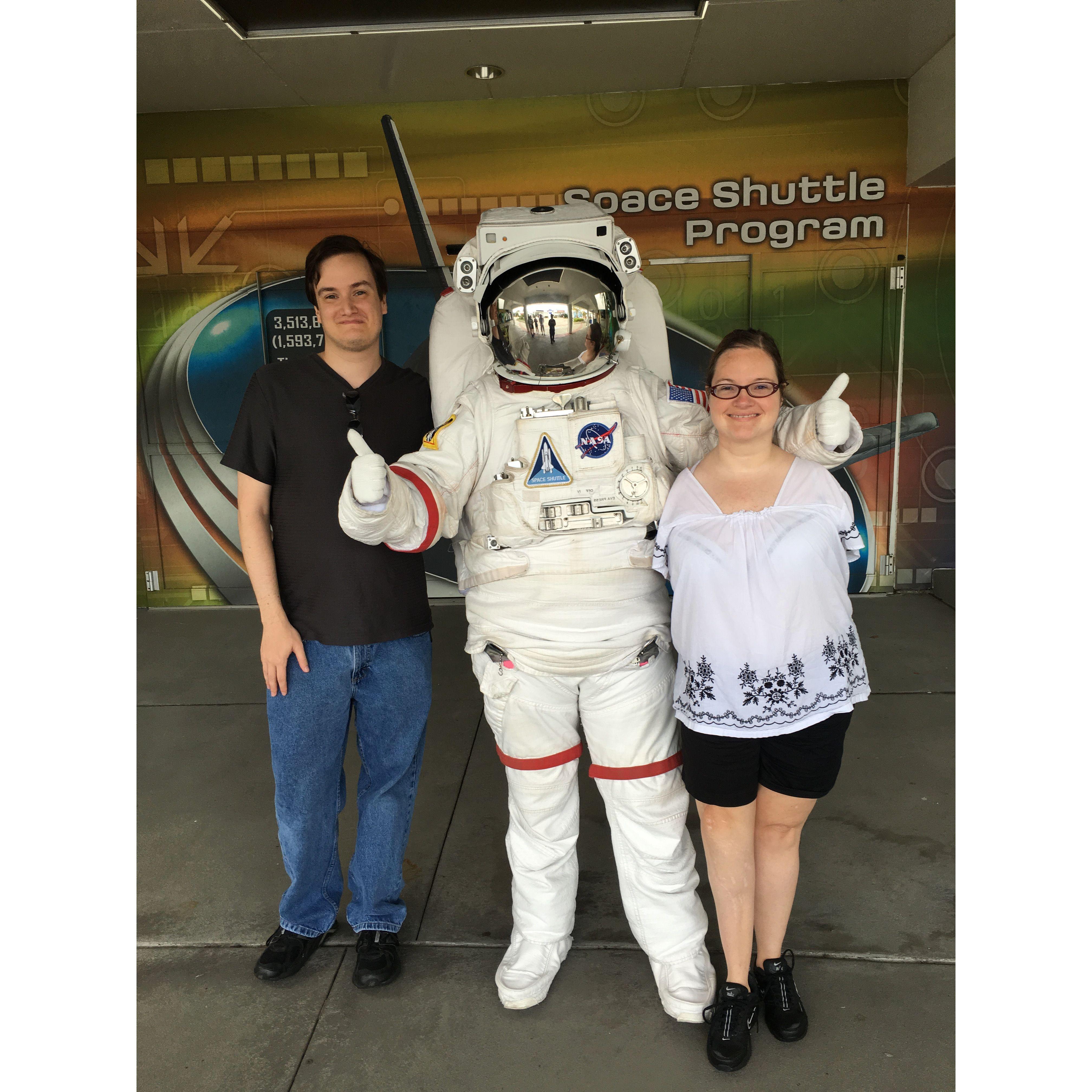 The couple pose with someone in an astronaut suit in between them. The astronaut has his arm around Olivia and is giving 2 thumbs up.
