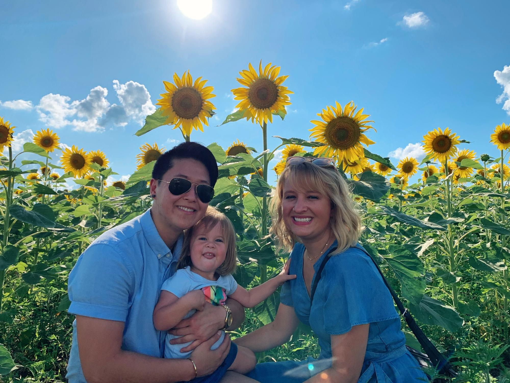 A beautiful trip with Saoirse & Ashley’s Mom to the Sunflower fields! Picture description: Ashley, Anhthu and Saoirse pose in front of a sunflower field, the sky is blue and the weather is bright.