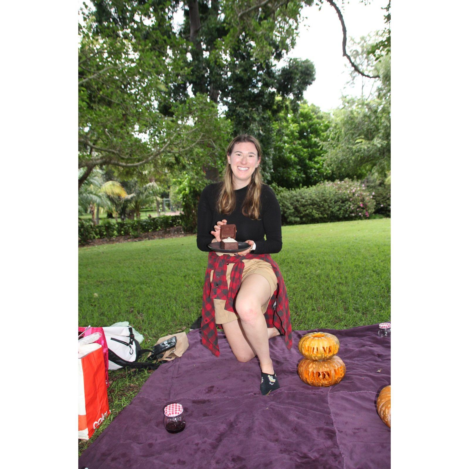 On March 24, 2025, it was Shana's turn to propose at the Brisbane Botanic Gardens. She planned a picnic complete with Caroline's favorite things — wine, cheese, pumpkin carving, and a chocolate ring box filled with carrot cake — and even carved the whole question herself!