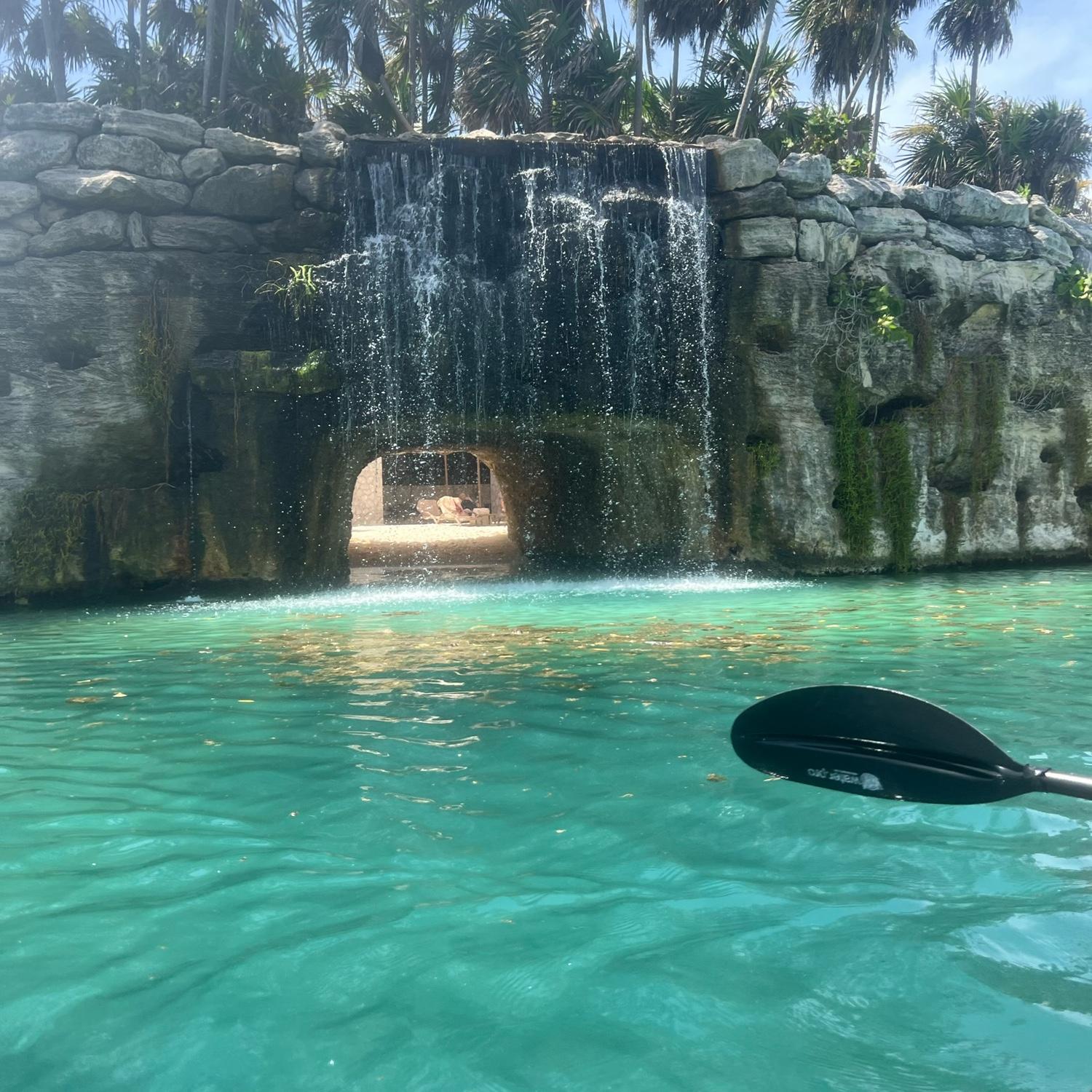 A waterfall and beautiful water you can see-through with a clear view of schools of little fish.