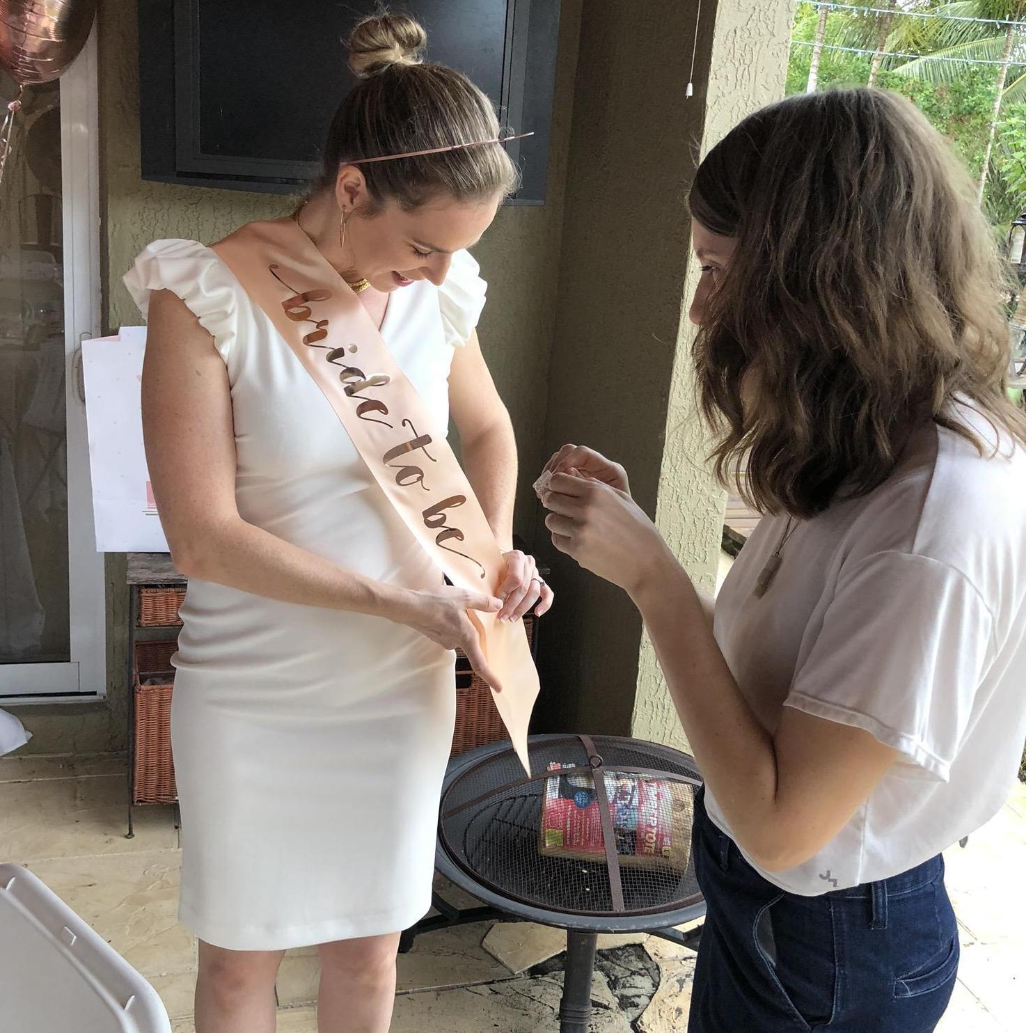 Kelsey and Kelley (sister/MOH) helping put Kelsey's sash on at Kelsey's Bridal Shower