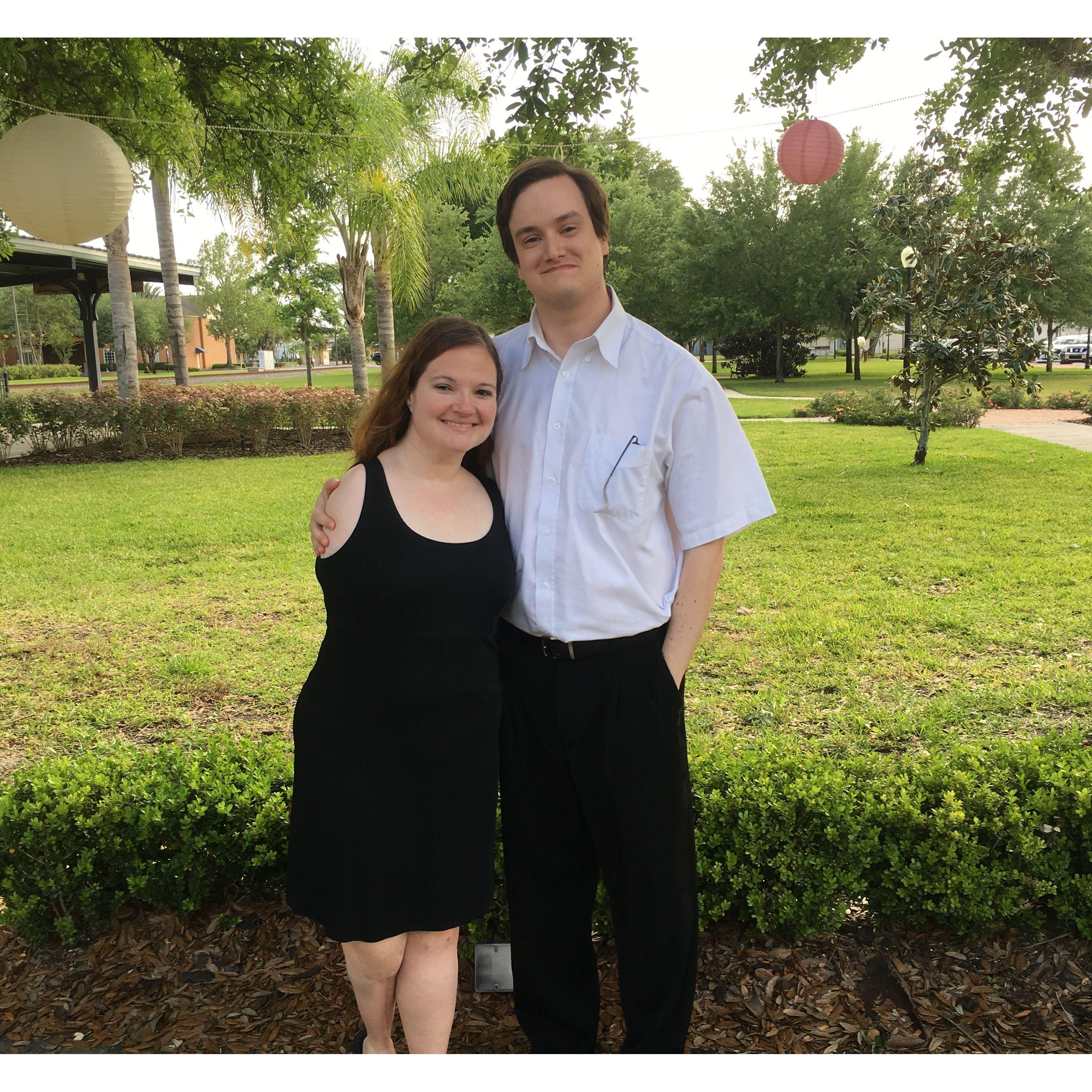 Olivia and Zac wearing black tie attire outdoors. They stand and smile below paper lanterns.