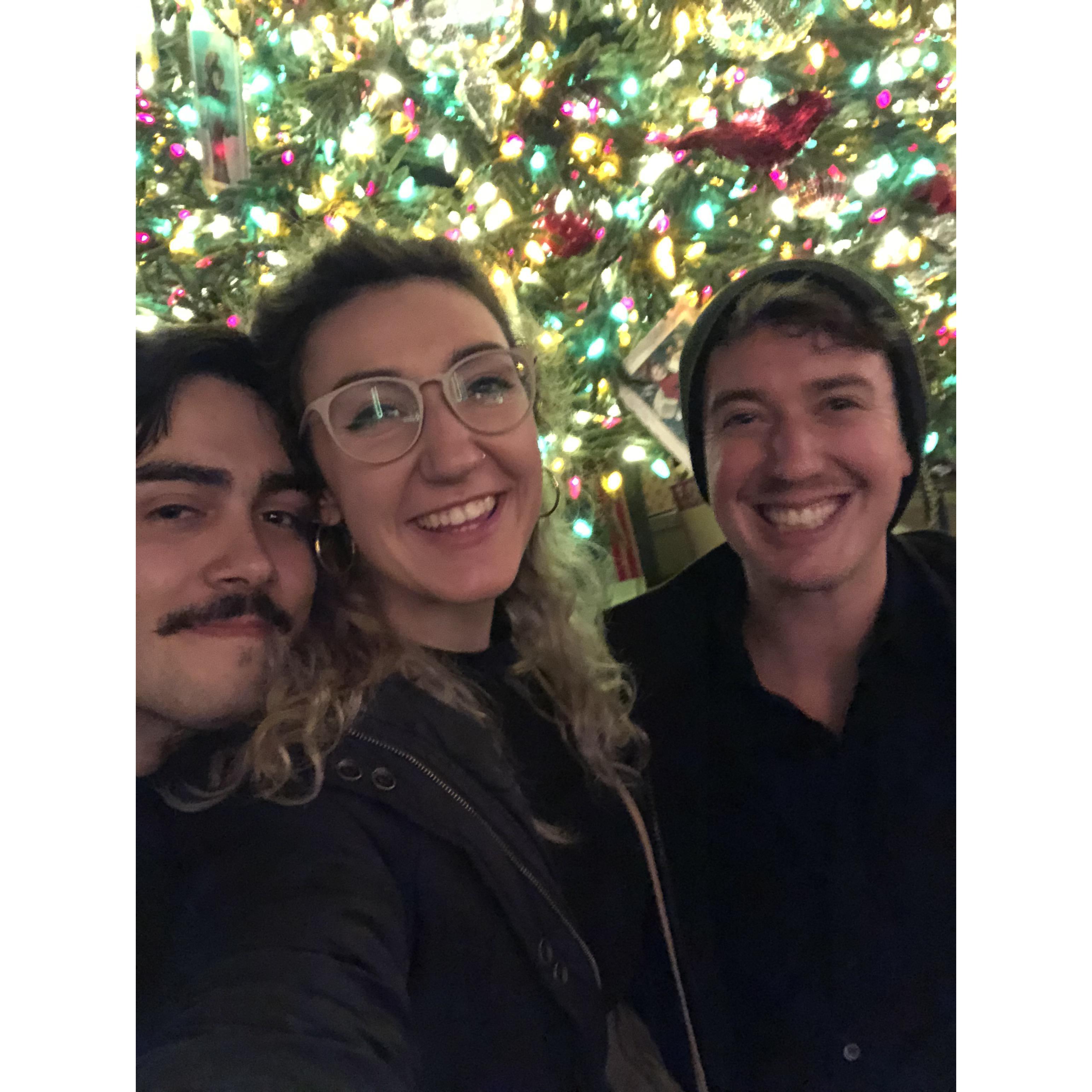 seth, kat, and benjy in front of a disneyland christmas tree at candlelight 2018