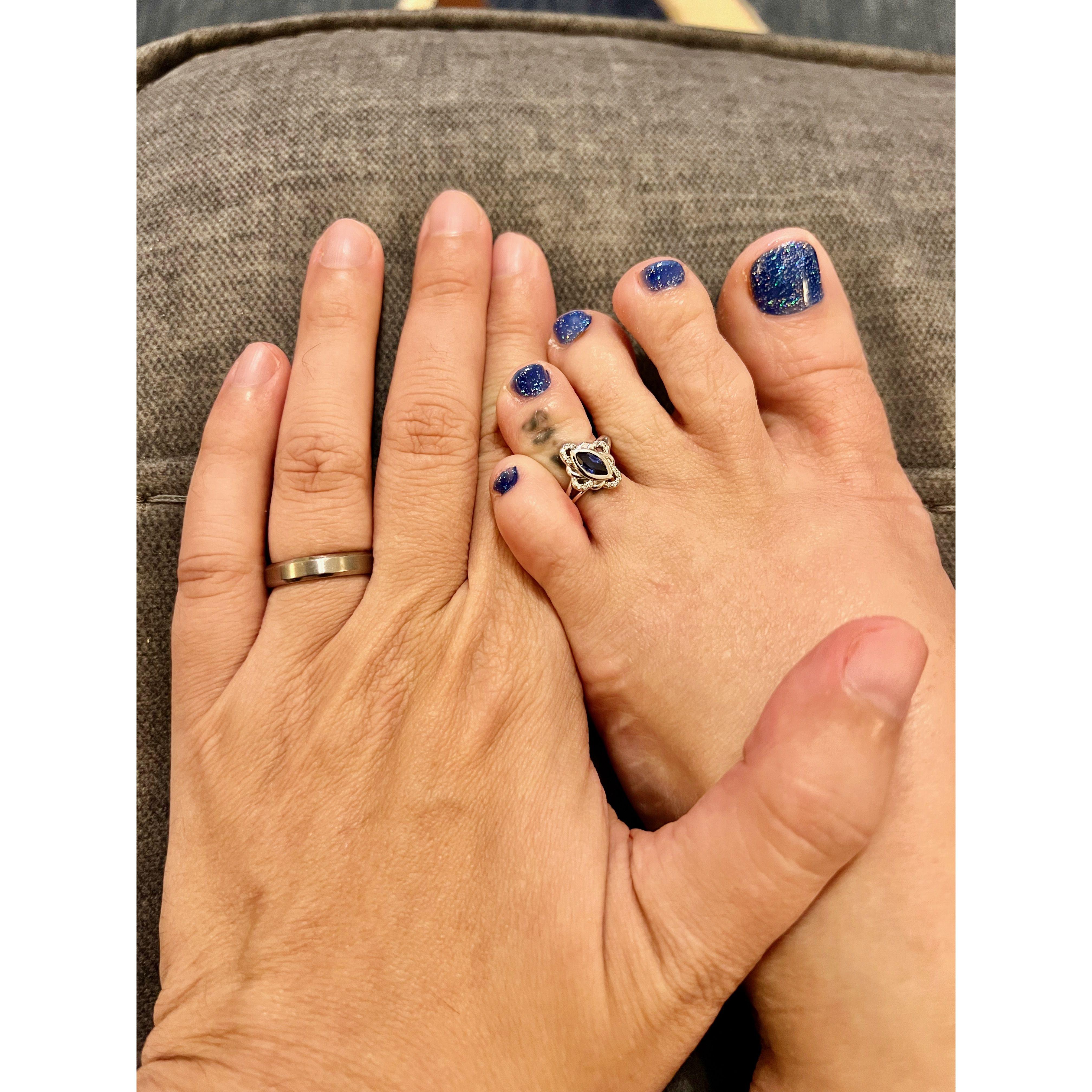 The couple’s wedding rings on Zac’s left hand and Olivia’s left foot. Zac’s is a classic titanium band. Olivia’s is silver with a large blue gem, which happens to match her blue nail polish.