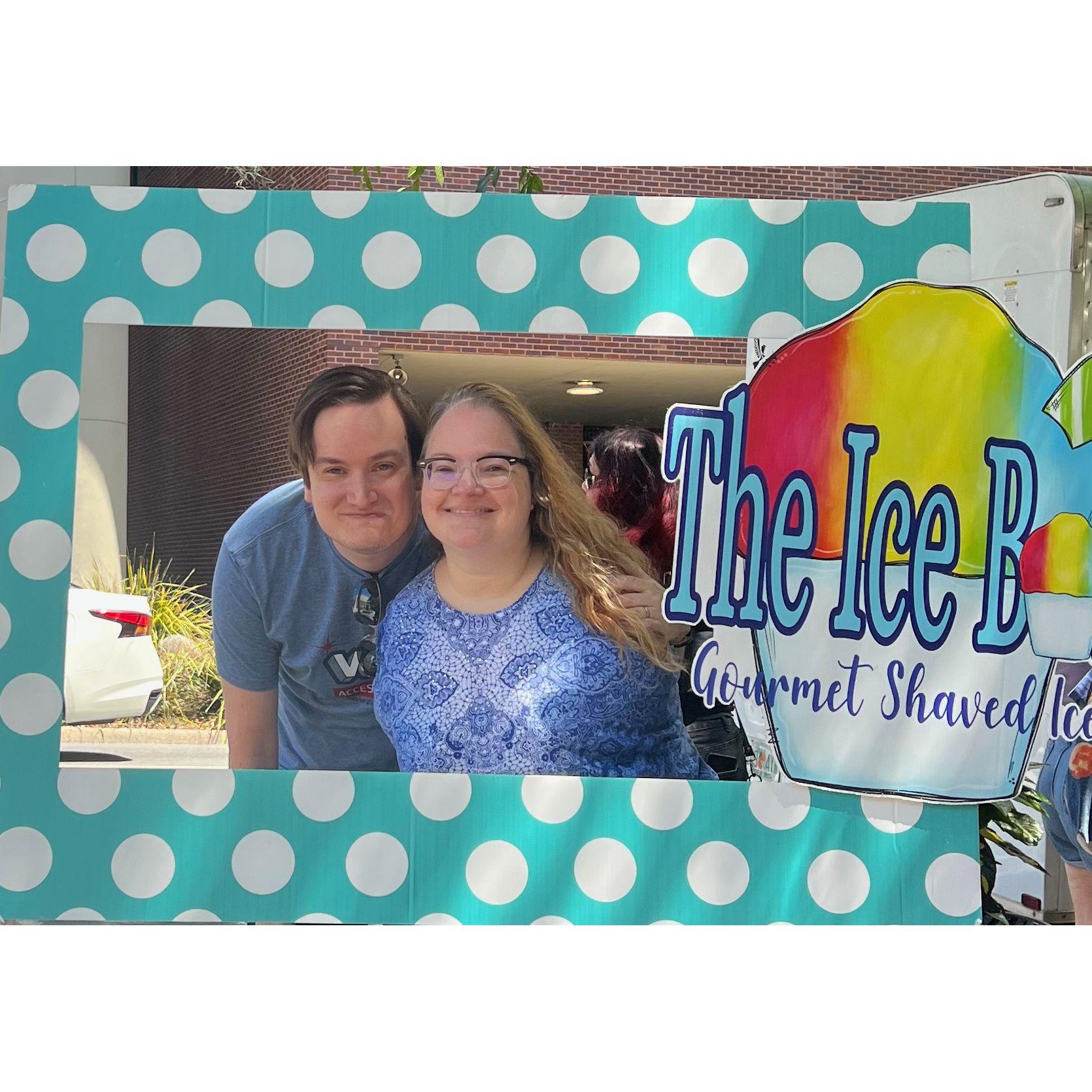 Zac and Olivia smiling and posing in a photo booth cut out for a shaved ice stand at Tallahassee Pride.