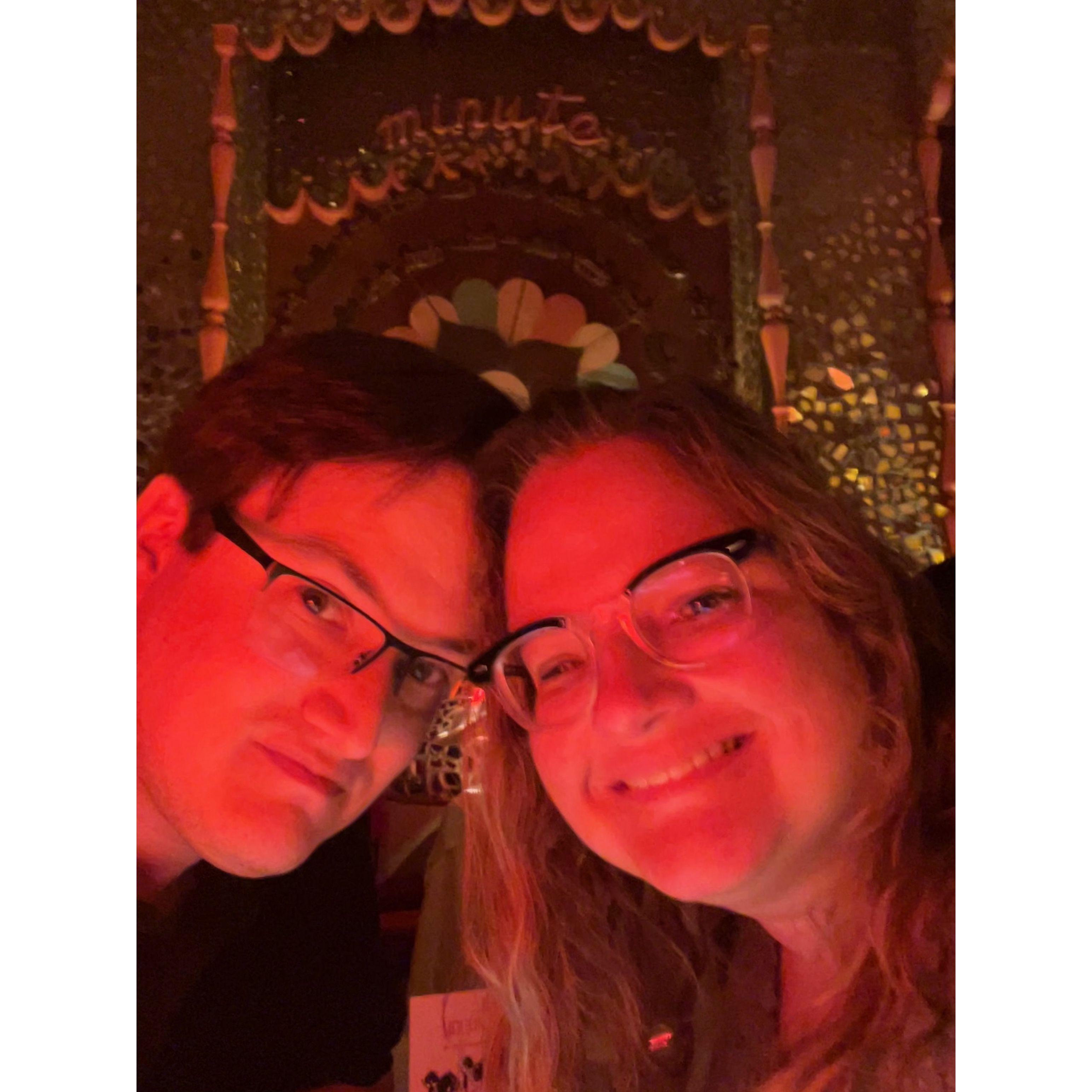 Selfie in a dark lit room with red lights lighting up their faces.