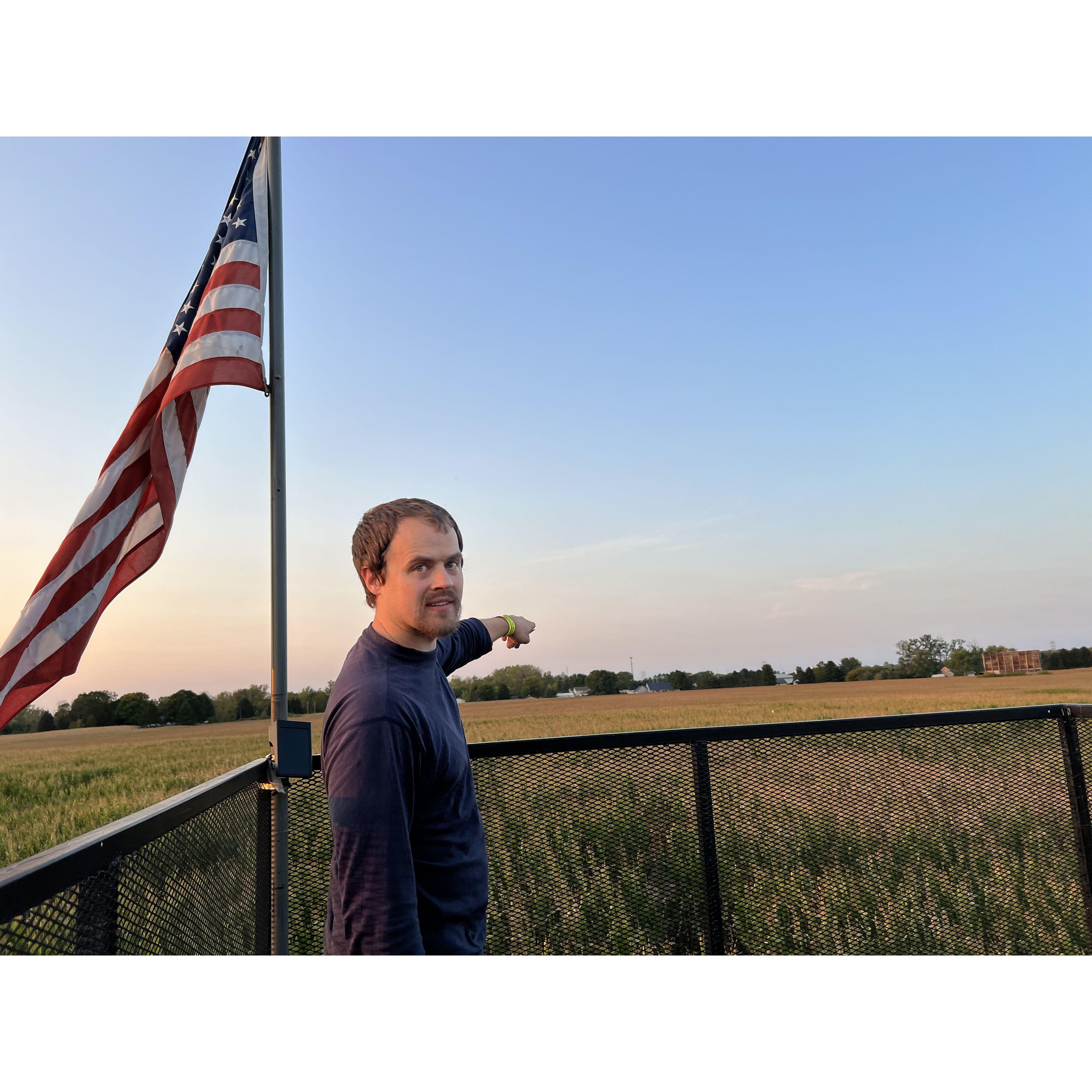Matt patriotically pointing over the top of a corn maze