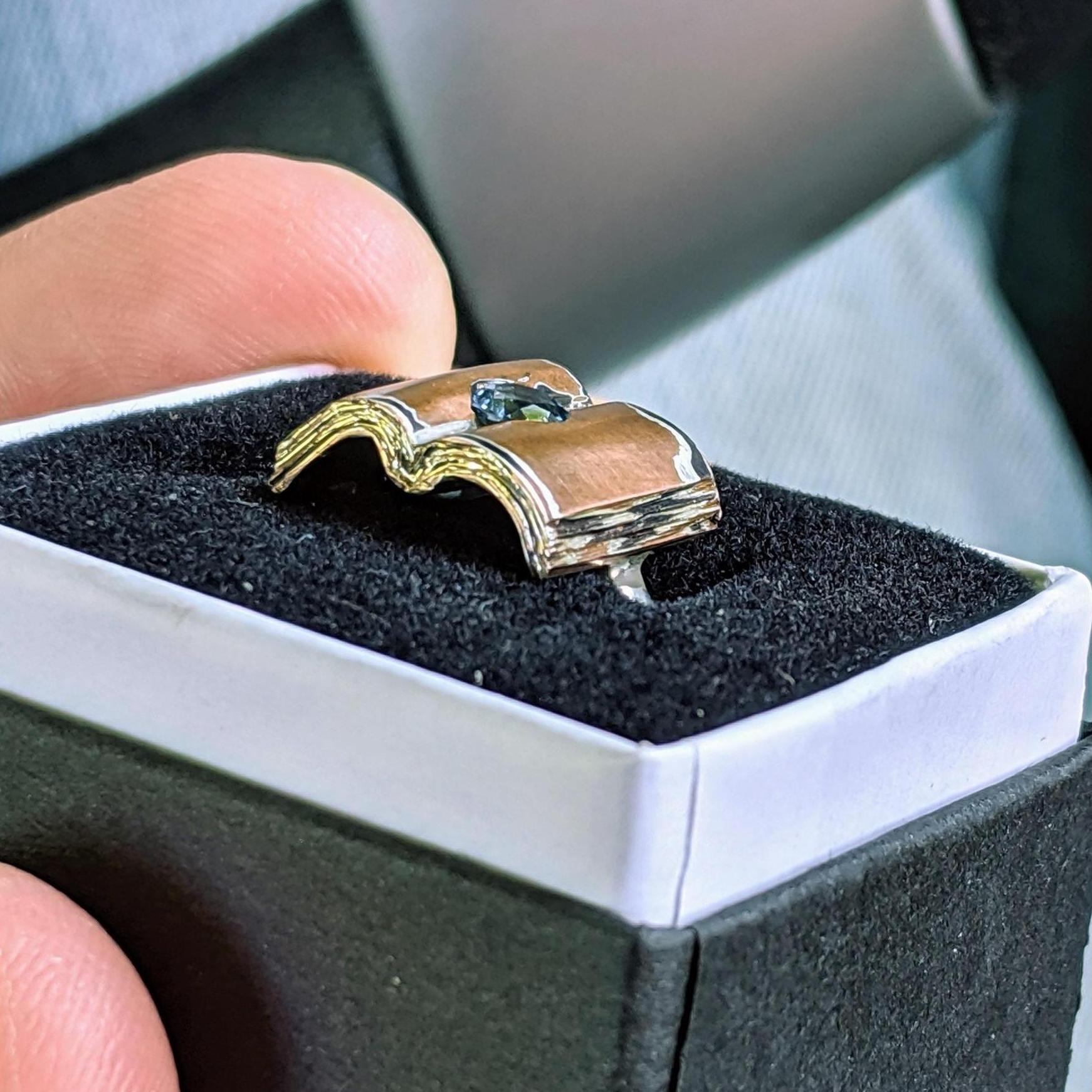 Eric had the idea for the ring for the past 3-4 years, and had it custom made at Magpie Jewlery in Wauwatosa, WI. It is mokume-gane with a river sapphire sourced from Montana.