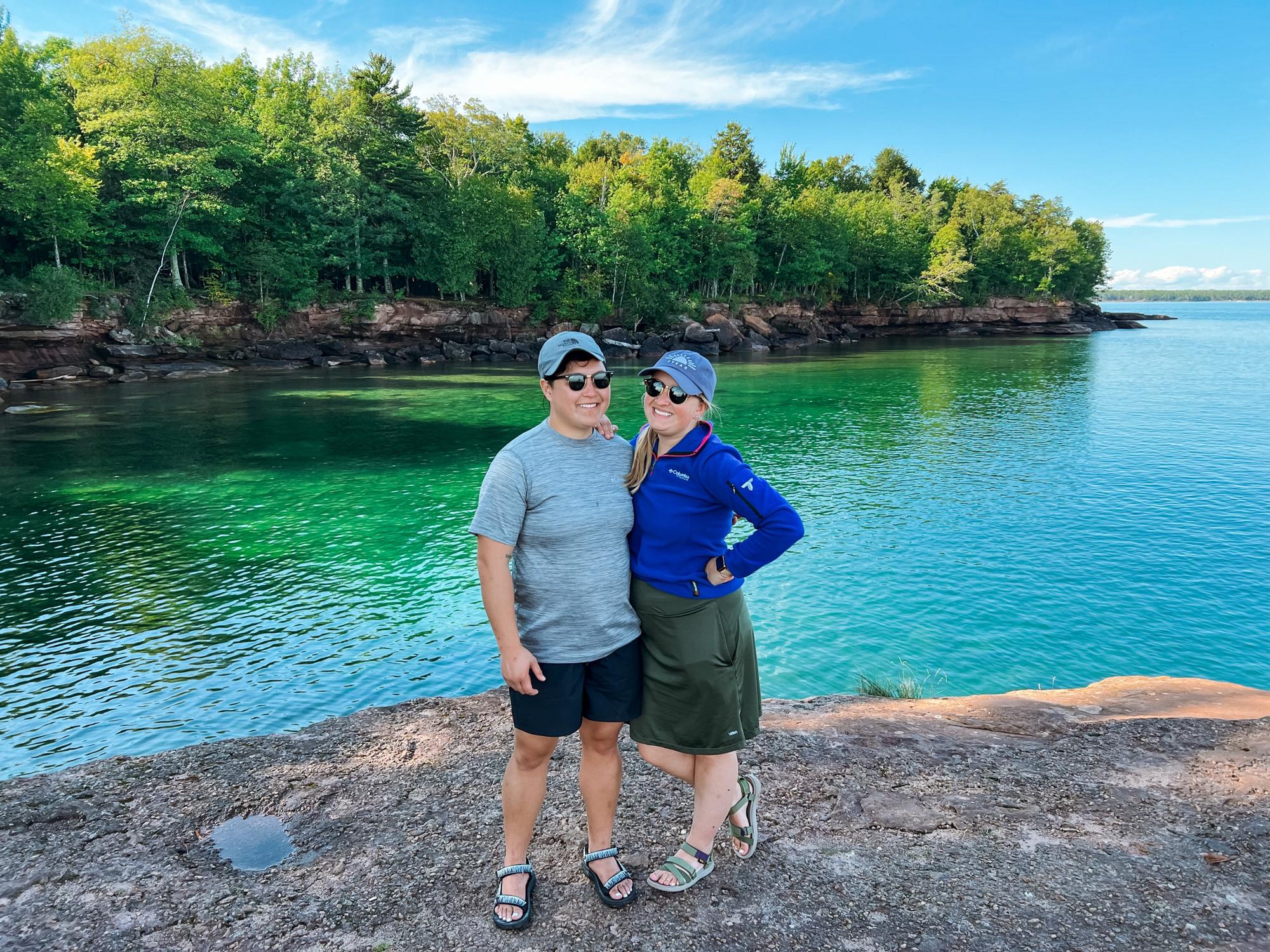 Our trip to the Apostle Islands in Sept. 2022 with Anhthu’s Matron of Honor Kelsey and her wife. Picture description: They pose in front of a rocky forest shoreline and the blue water of Lake Superior