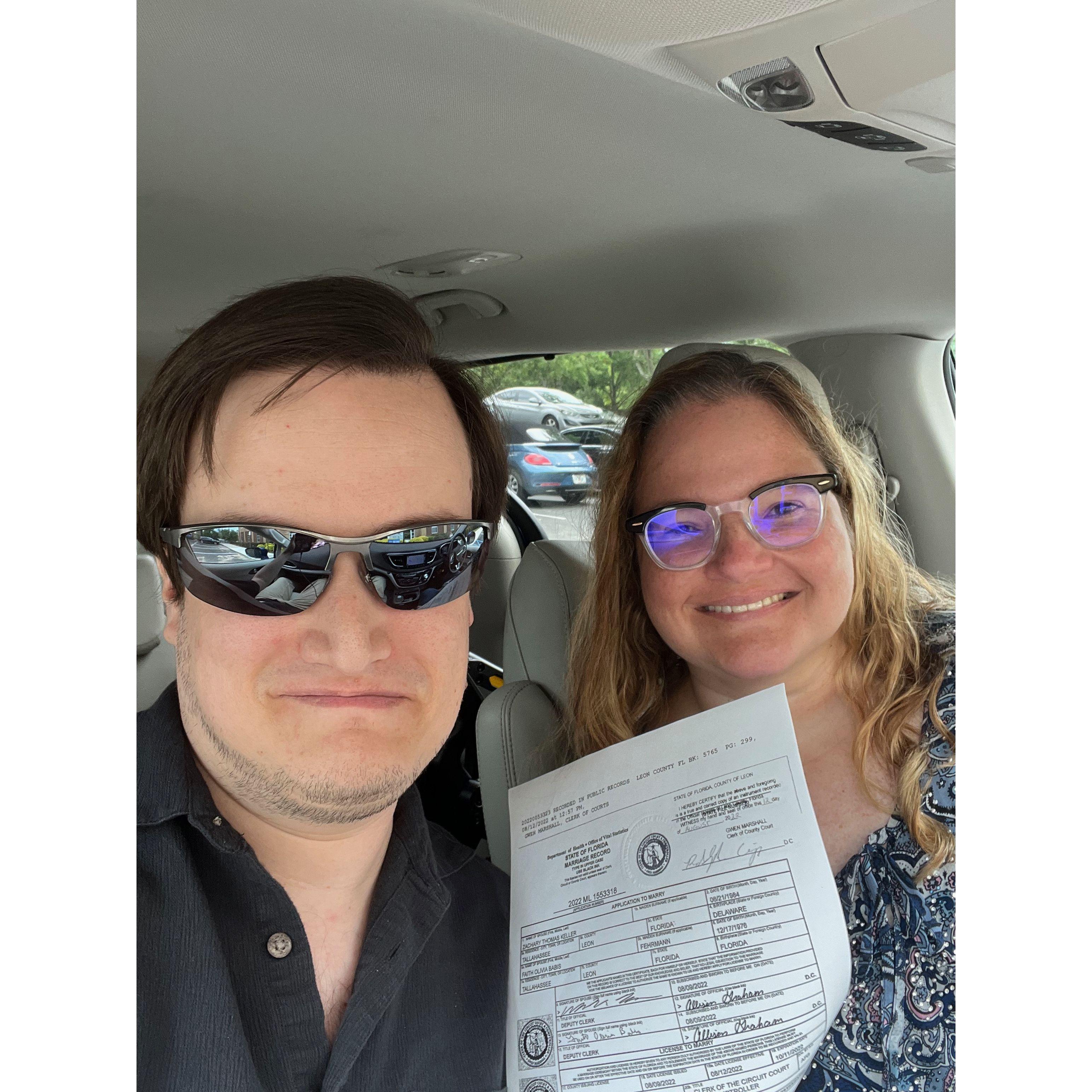 Zac and Olivia smiling holding a marriage certificate.