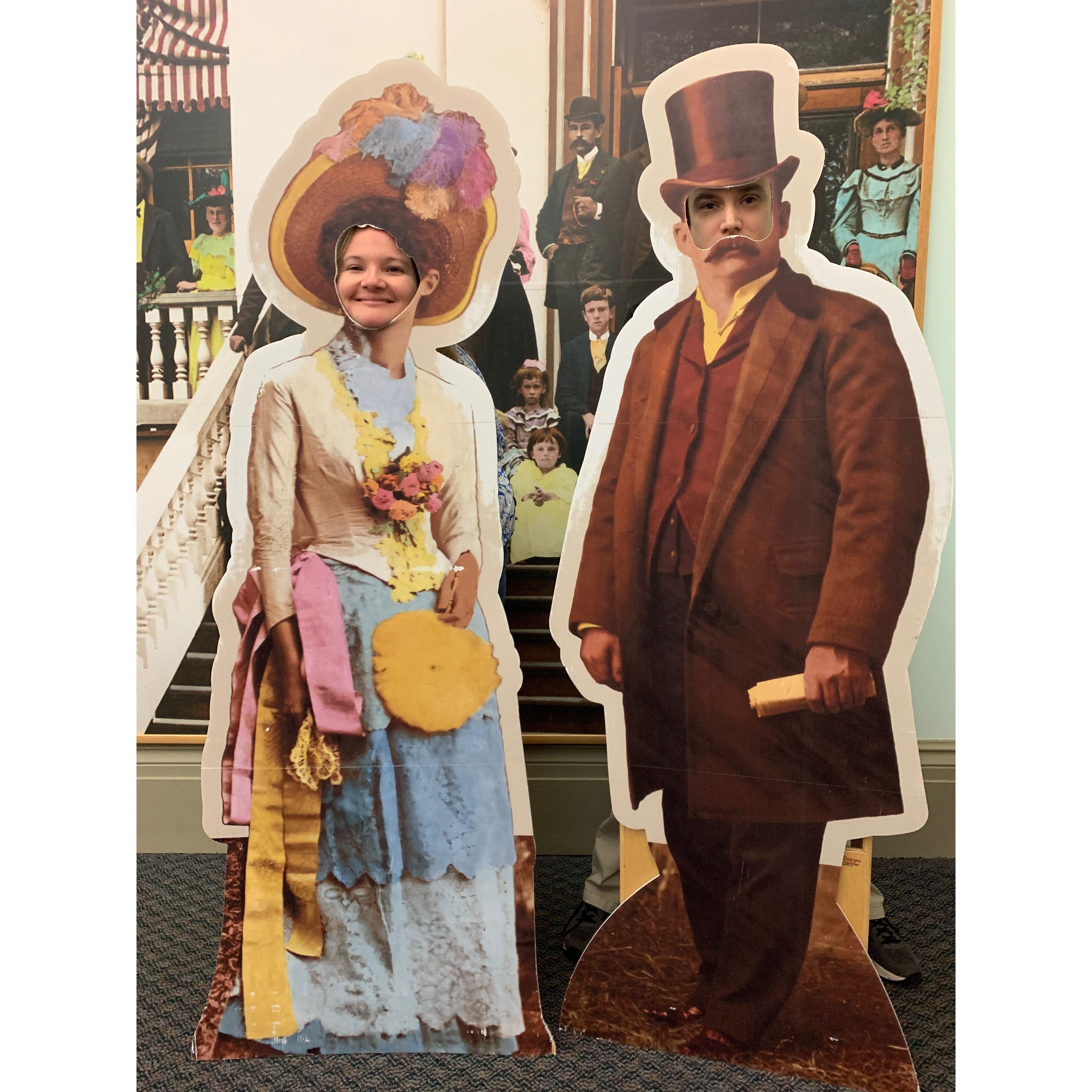 The couple putting their faces in the holes of cardboard cutouts of people wearing old timey outfits at the FL Historic Capitol museum.