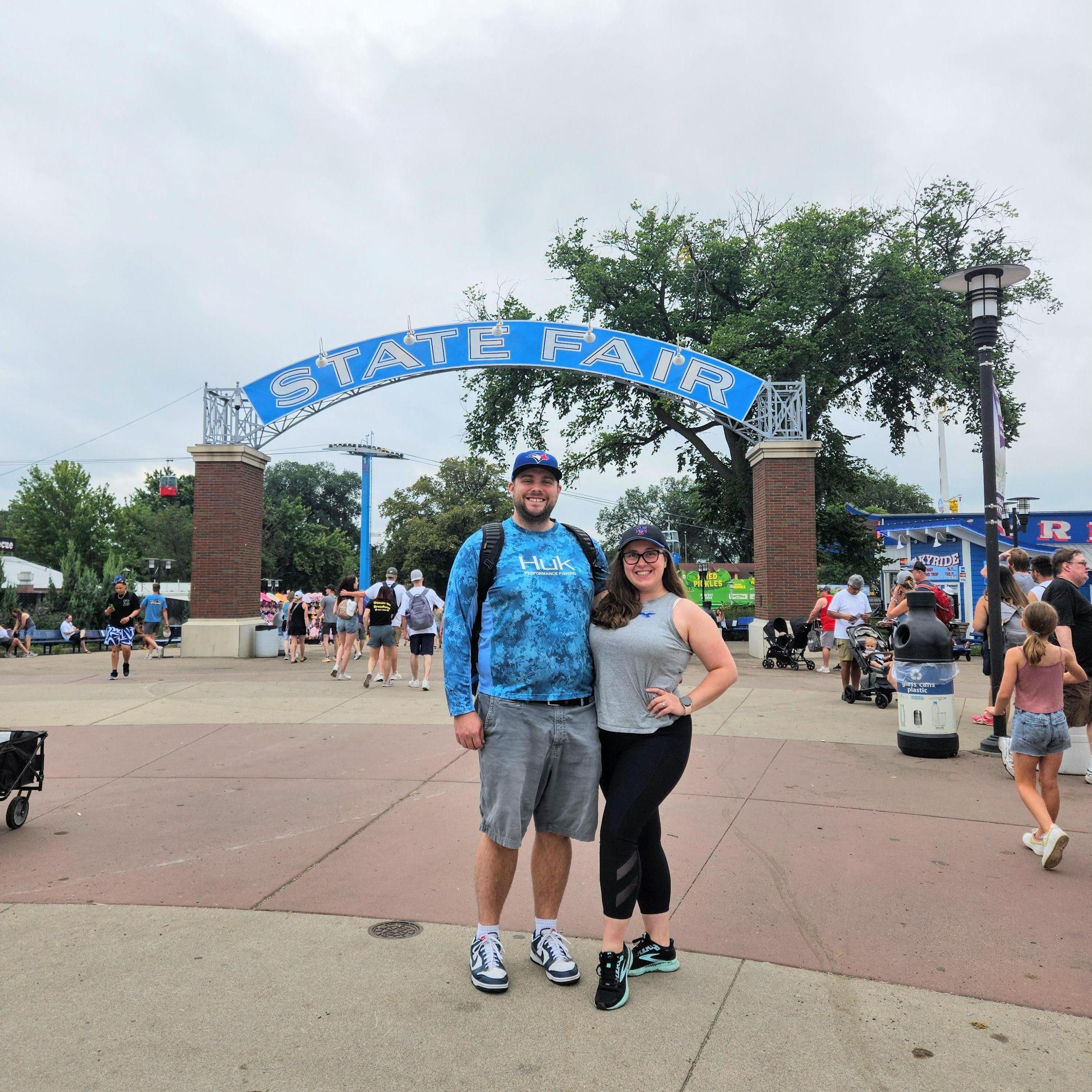 Our favorite place in the state - the MN State Fair!  Alt text: Maeghan and Keiran standing underneath the MN State Fair entryway