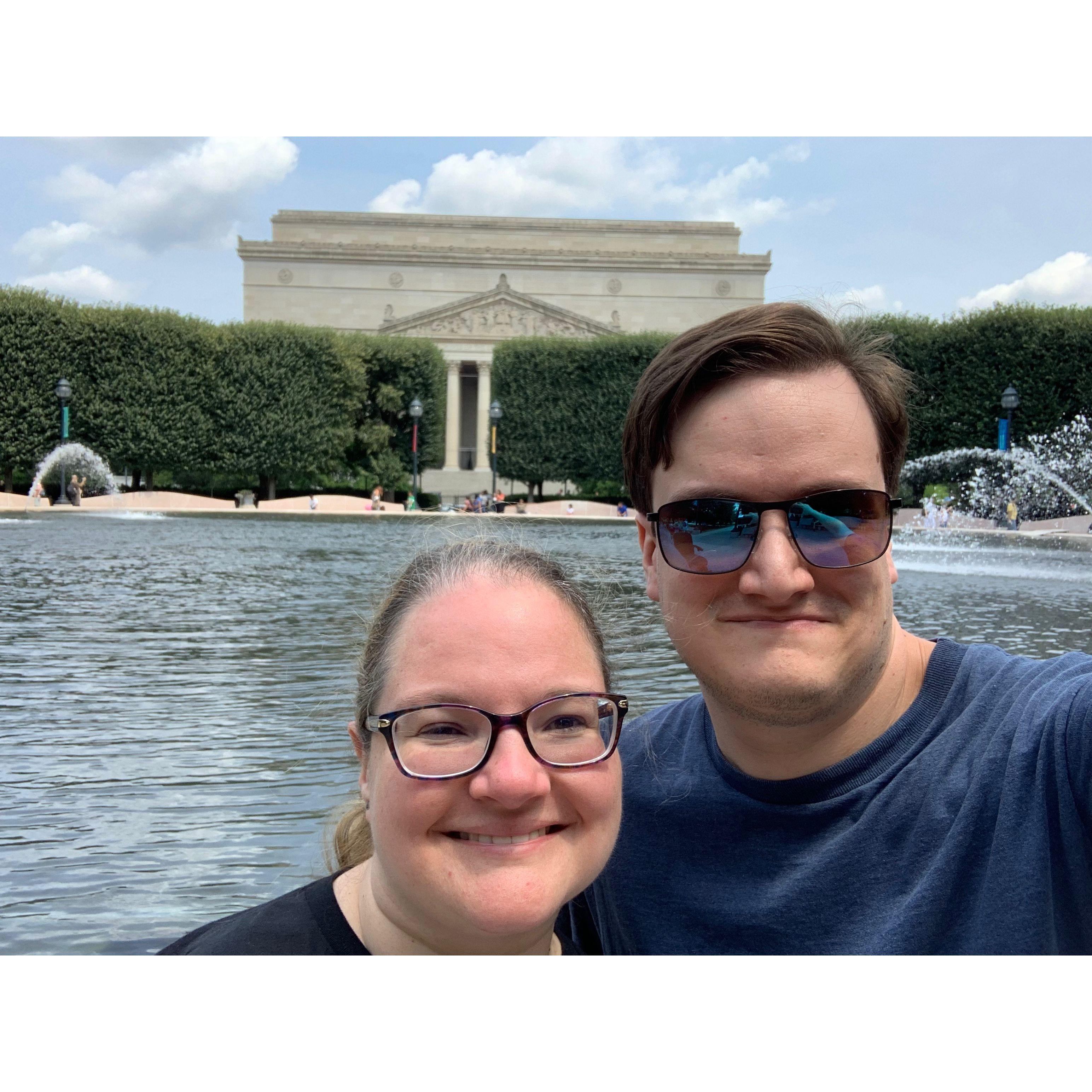 Selfie in front of a large pond. The pond sits in front of the National Gallery of Art, a classical looking building.