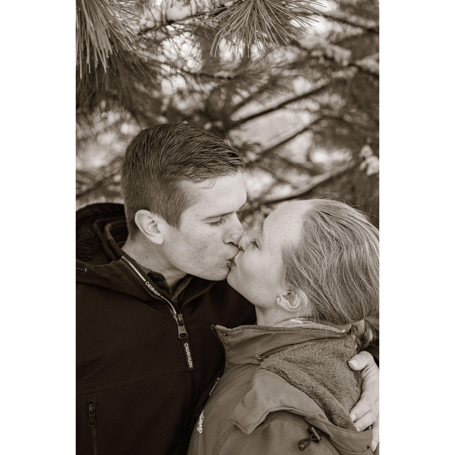 Grayscale smooches under a pine.