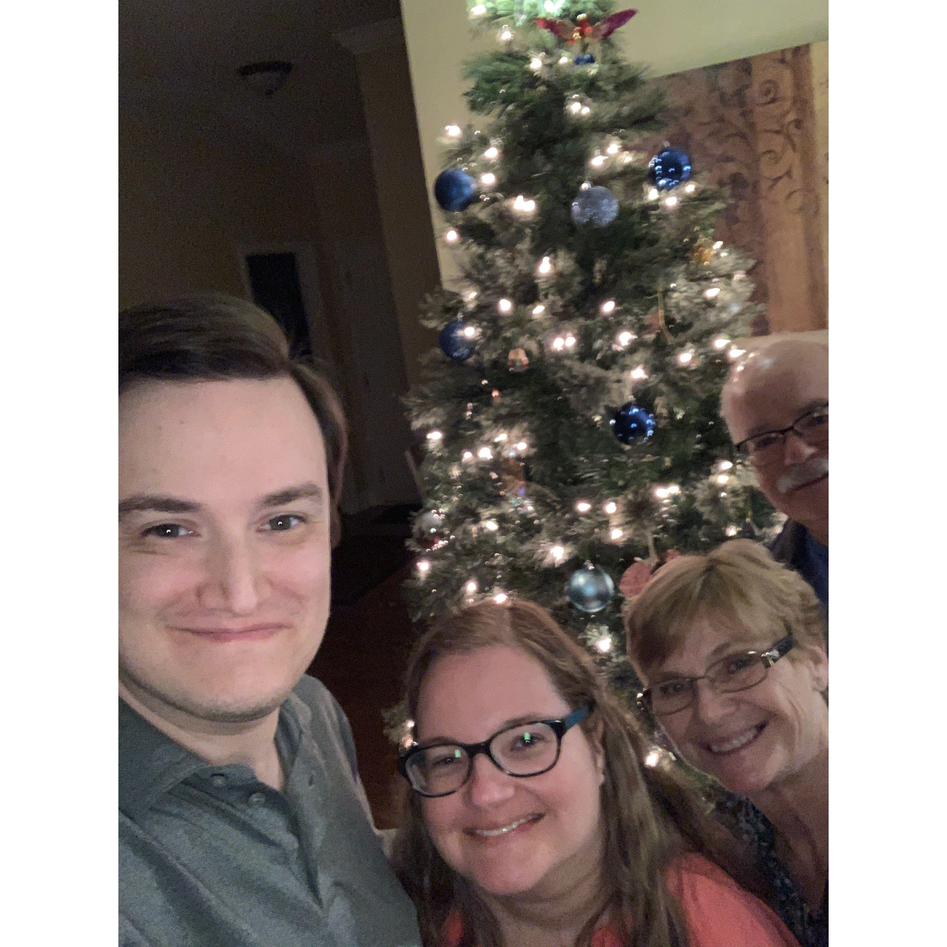 Selfie with Olivia’s aunt and uncle. They stand in front of a Christmas tree with lots of ornaments and bright lights
