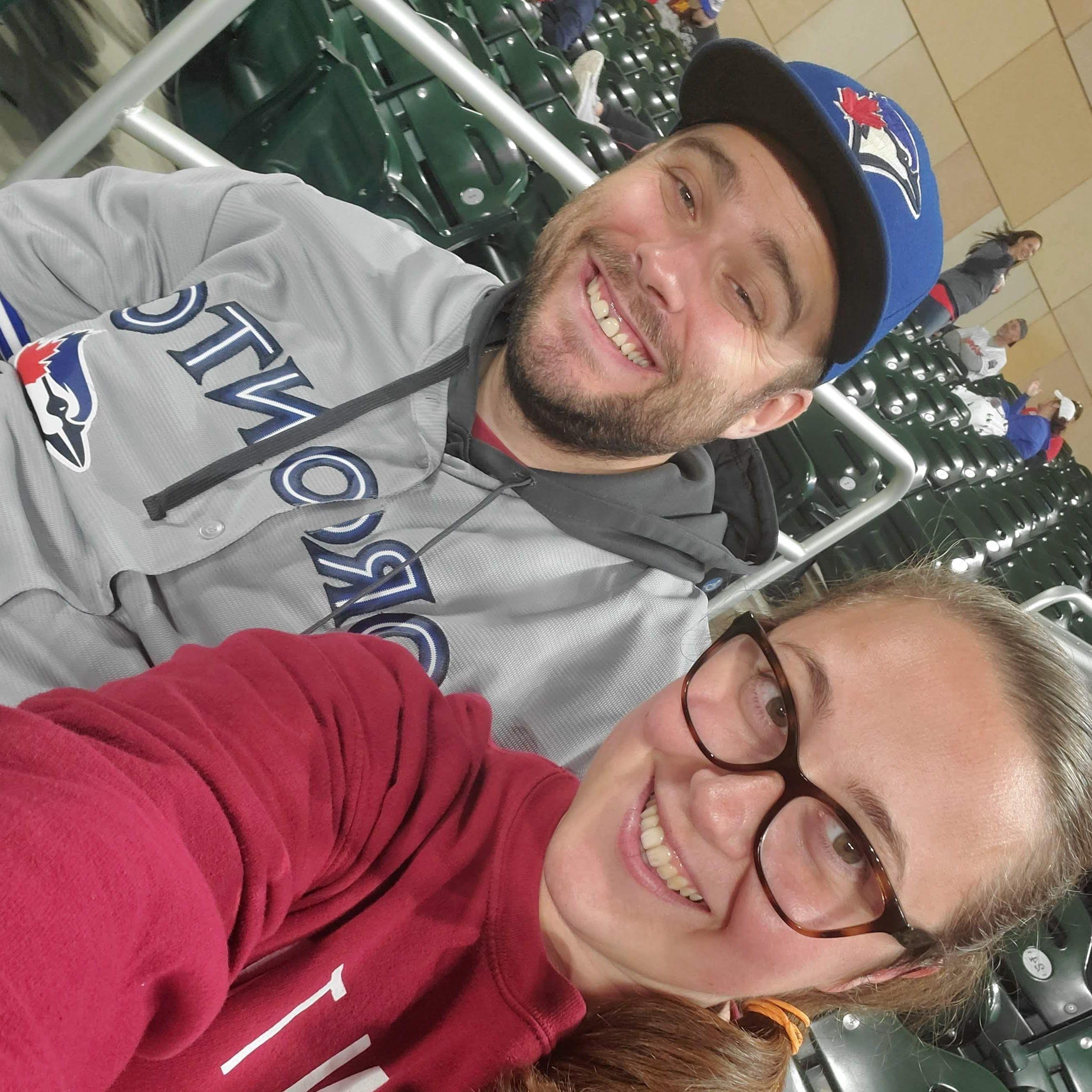 Alt Text: a selfie of Maeghan and Keiran at a Twins game, Keiran wearing Toronto Blue Jays gear