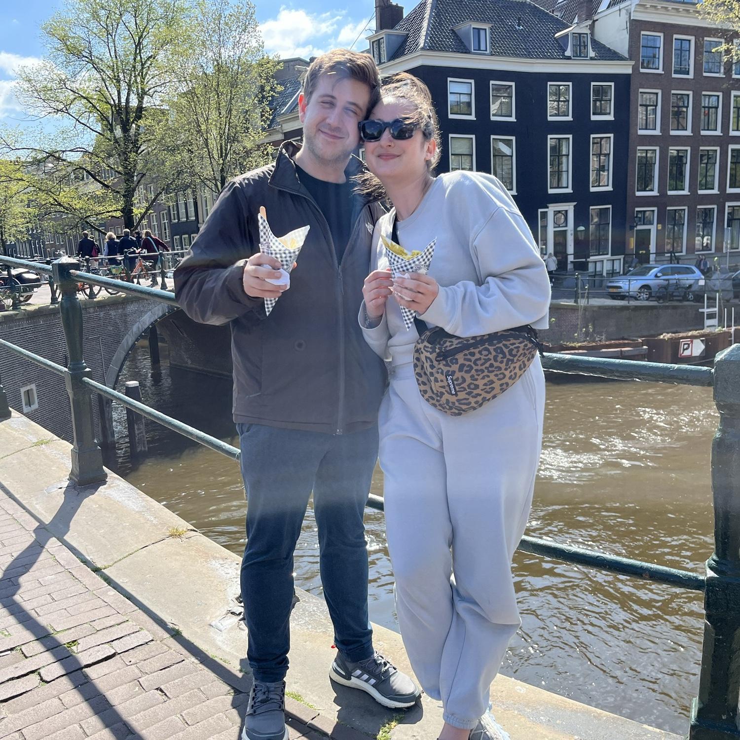 Hillary and Jay in Amsterdam eating french fries on a canal in April 2022