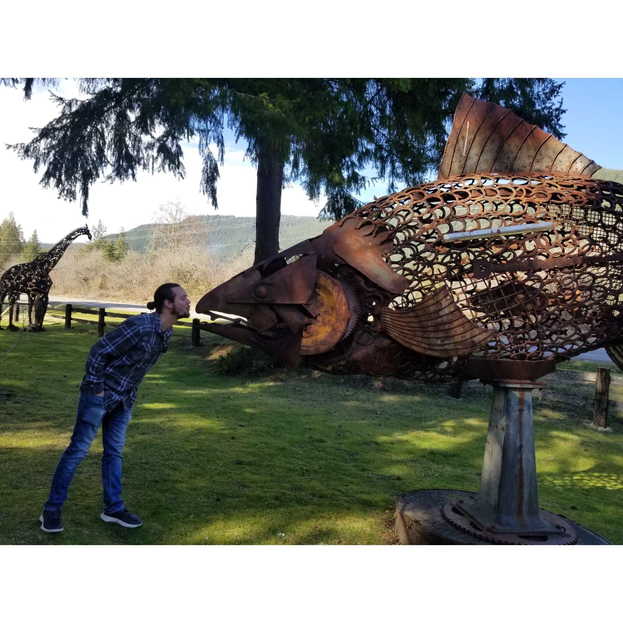 Ryan kissing a giant metal salmon at the same outdoor sculpture park