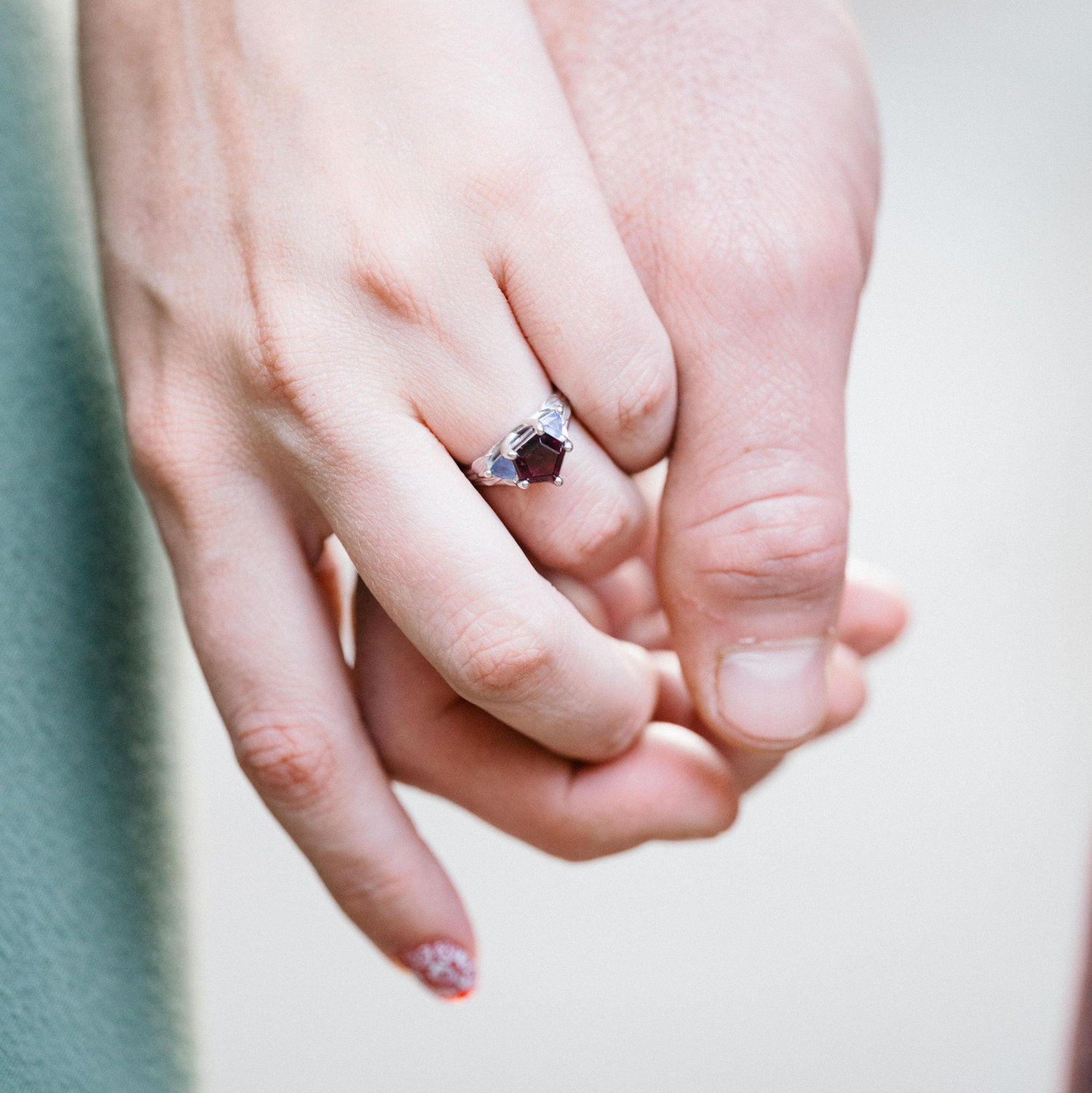 Mac designed their ring! The center stone is a pentagon star-cut rhodolite (a variety of garnet) and was faceted by their paternal grandfather, Dr. Smith. The flanking stones are tanzanites.