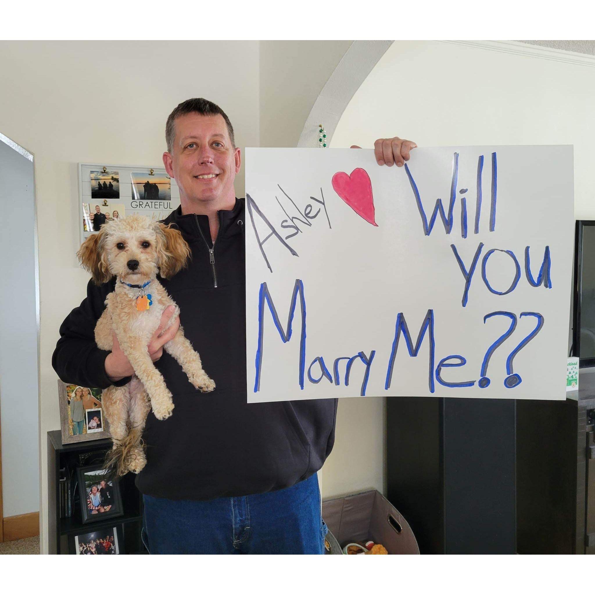 March 2023 · Mike at home with Brooks holding up the sign he made himself for the proposal! This was the photo used on the screen for the proposal, and Ashley loves he included Brooks.