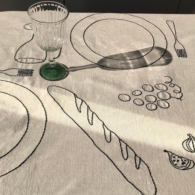 Hand-embroidered tablecloth with plates, fork, knife, wine glasses, baguette, lemon, grapes, tomatoes, figs