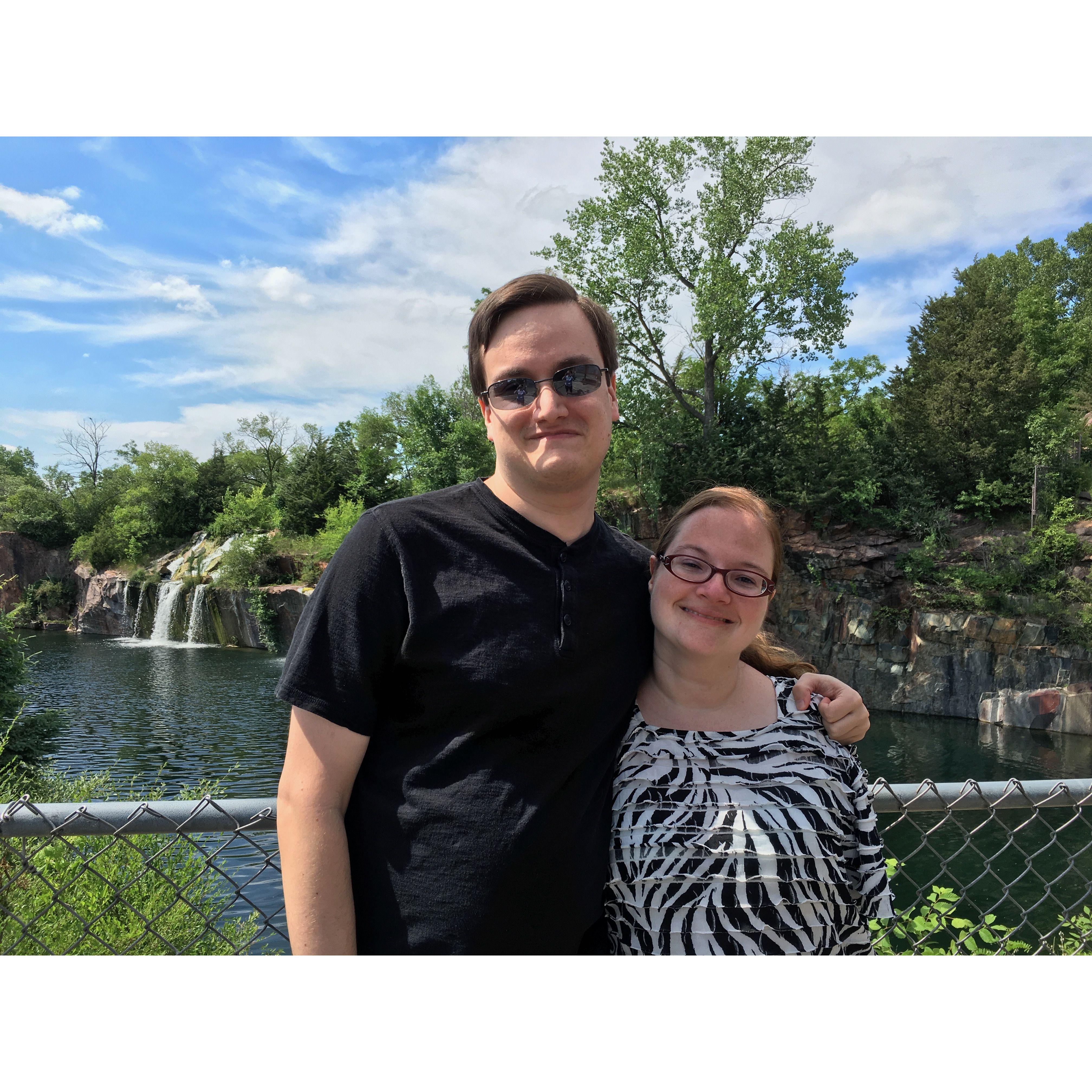 The couple standing outdoors with a waterfall and lake behind them
