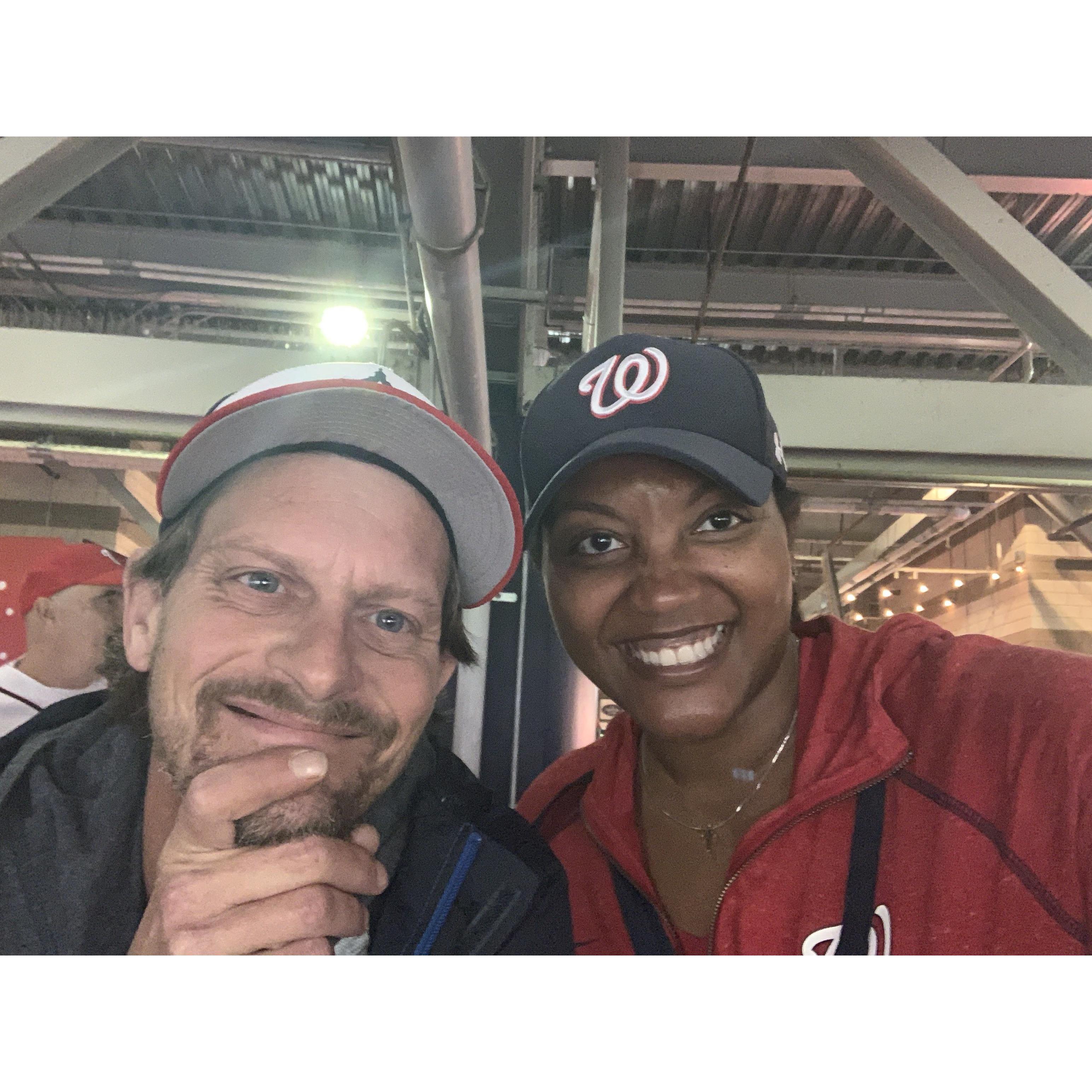 Eric is trying to watch baseball while Adrienne wants to take a picture instead.
