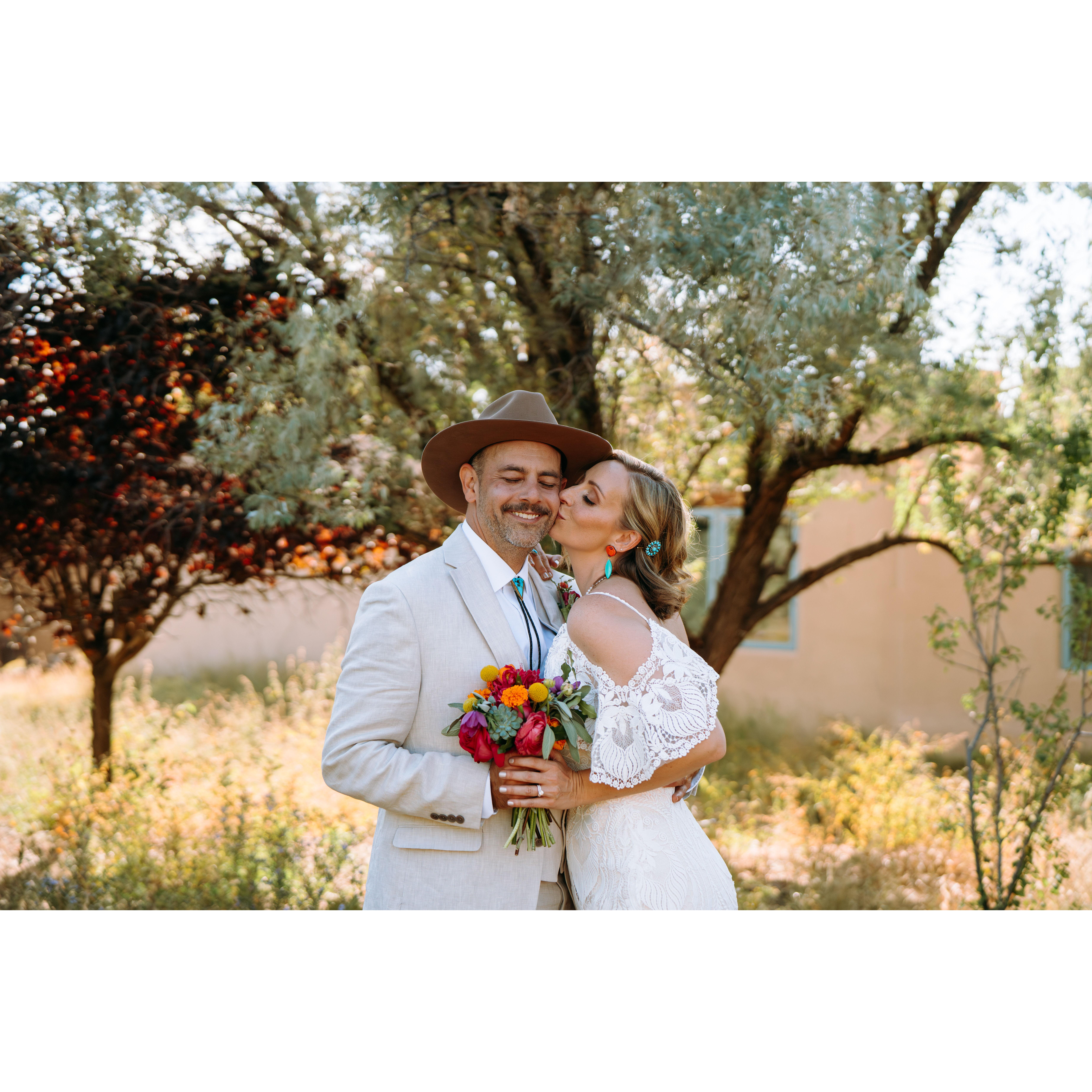 Jenn kisses Shae's cheek as he holds her hand by his chest with her flower bouquet