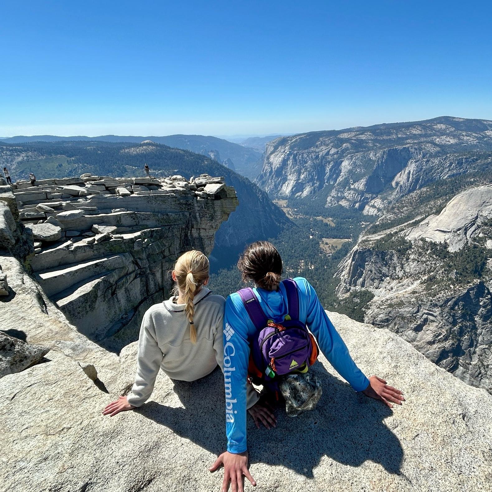 Ian and Callie hang their legs off the top of Half Dome in Yosemite National Park.
