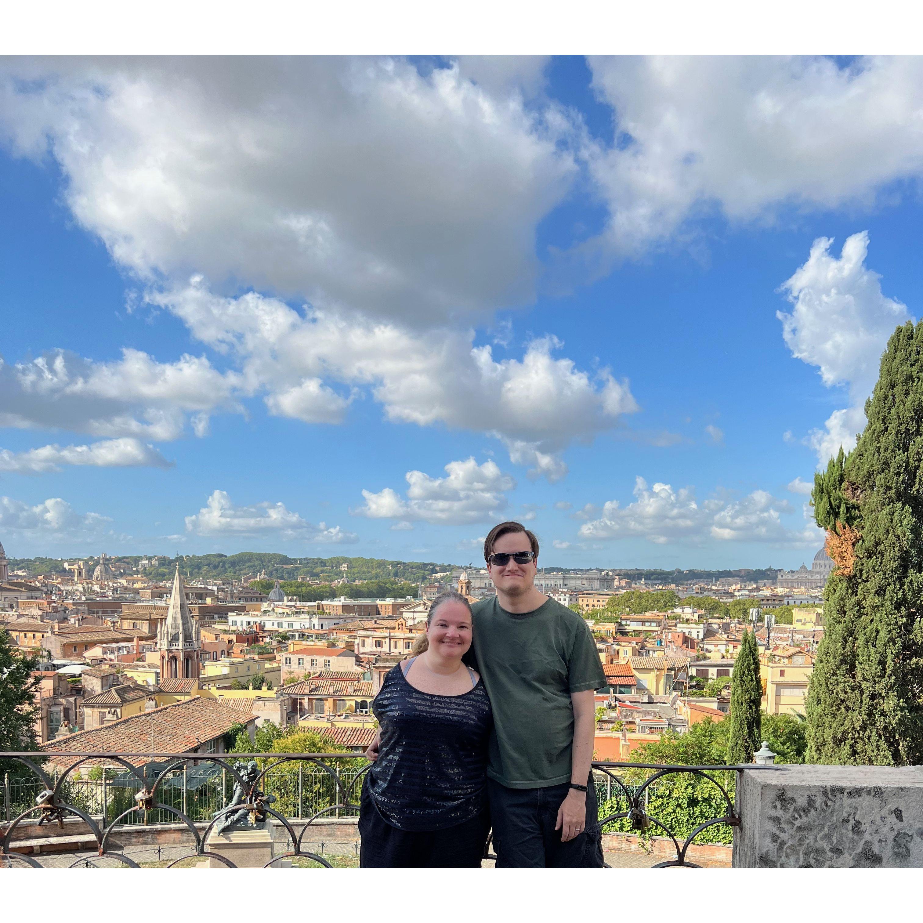 The couple standing at a viewpoint with the city of Rome behind them.