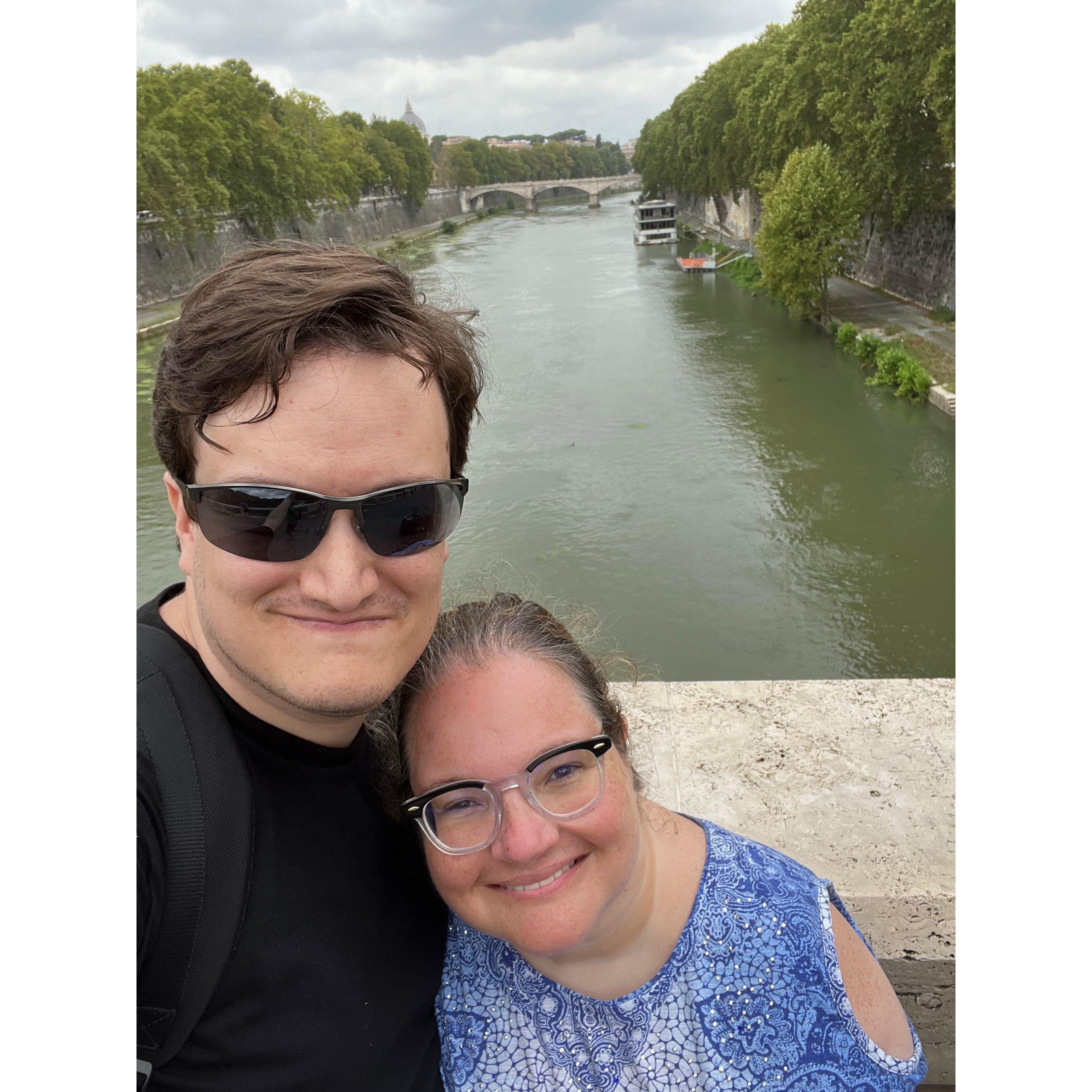Selfie on a bridge above the Tiber river. Lush trees spill over the river’s walls.