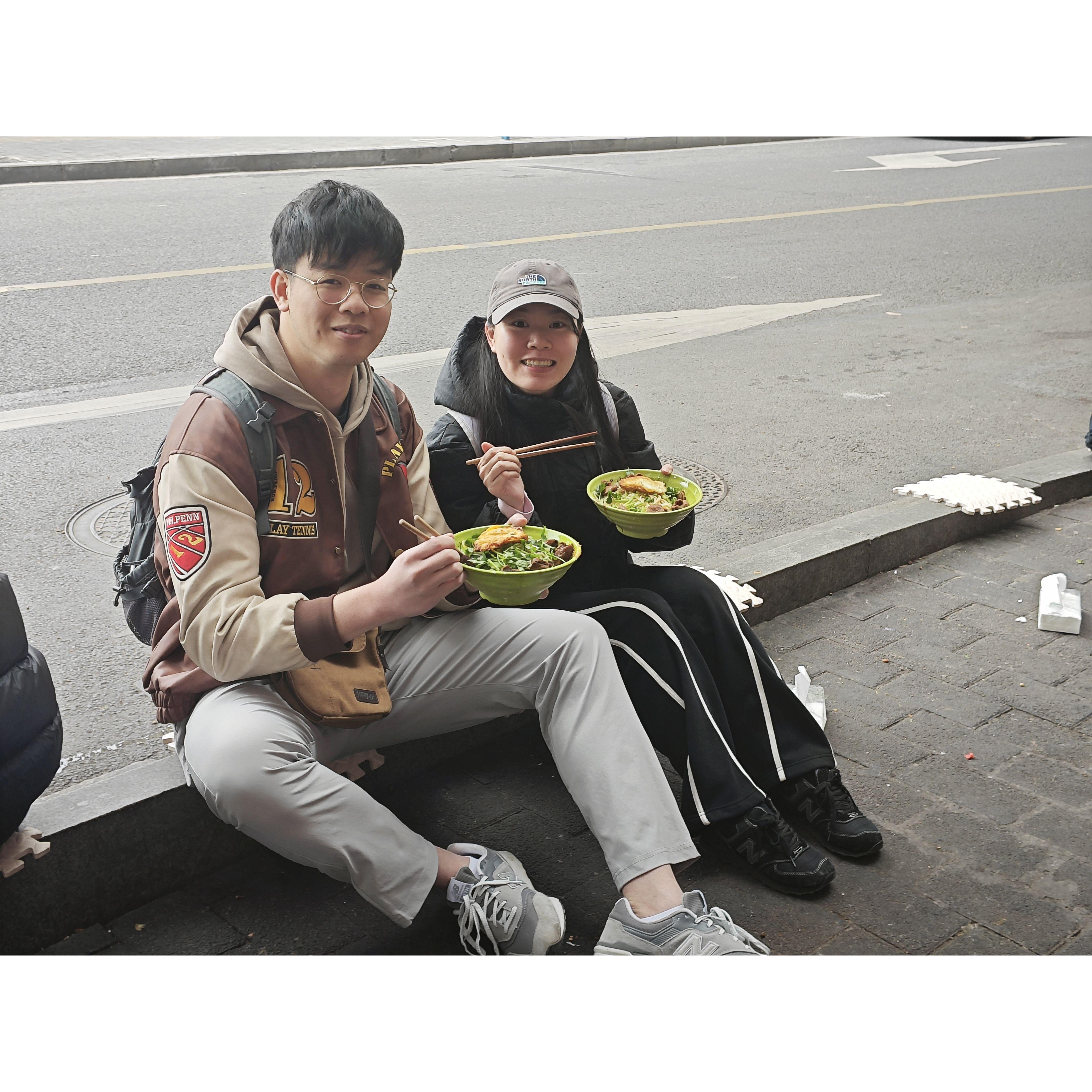 In Chongqing, our first time eating noodles sitting on the side of the road. Super spicy, lots of 流鼻涕