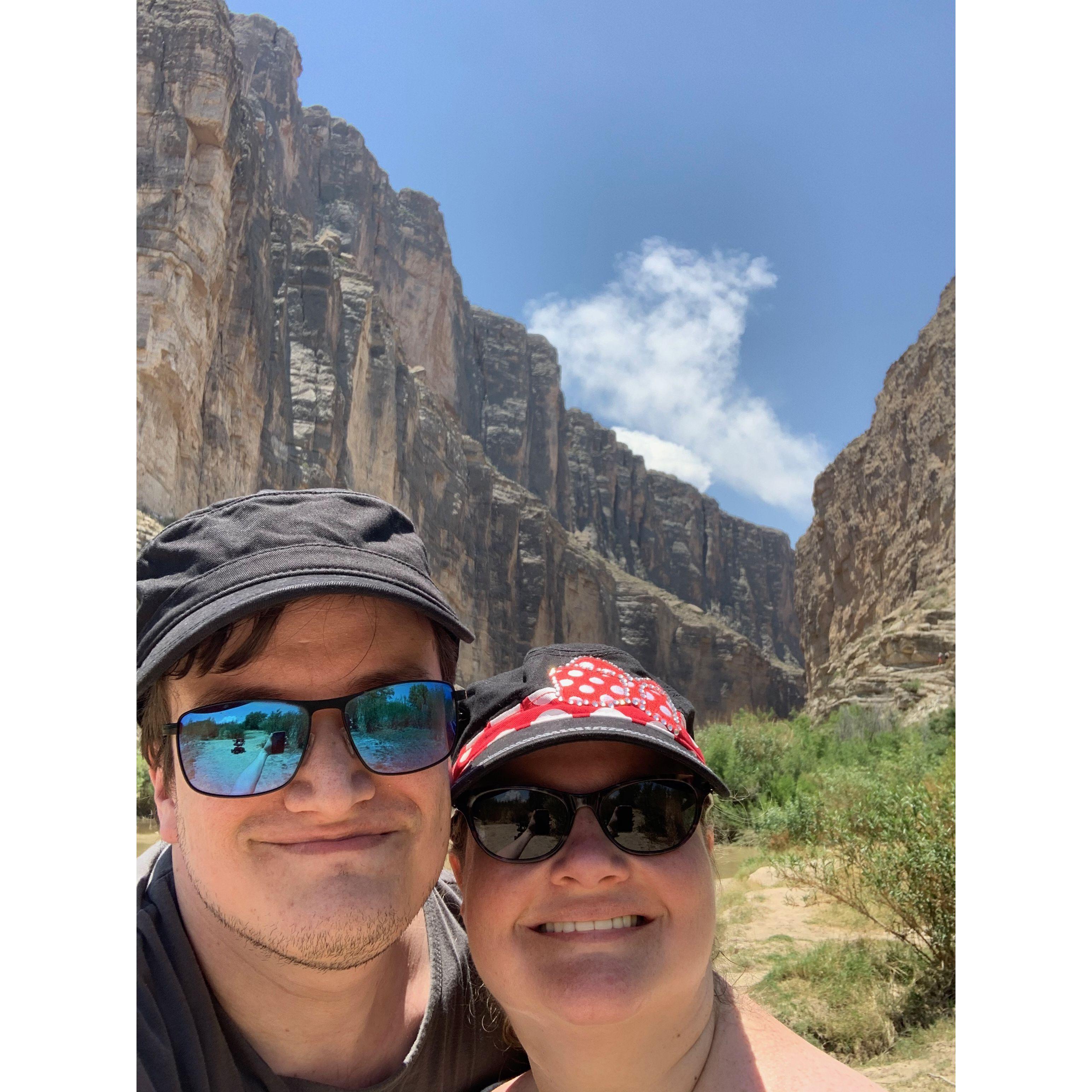 Selfie in a canyon at the Rio Grande. Light blue skies with wispy clouds are behind them.