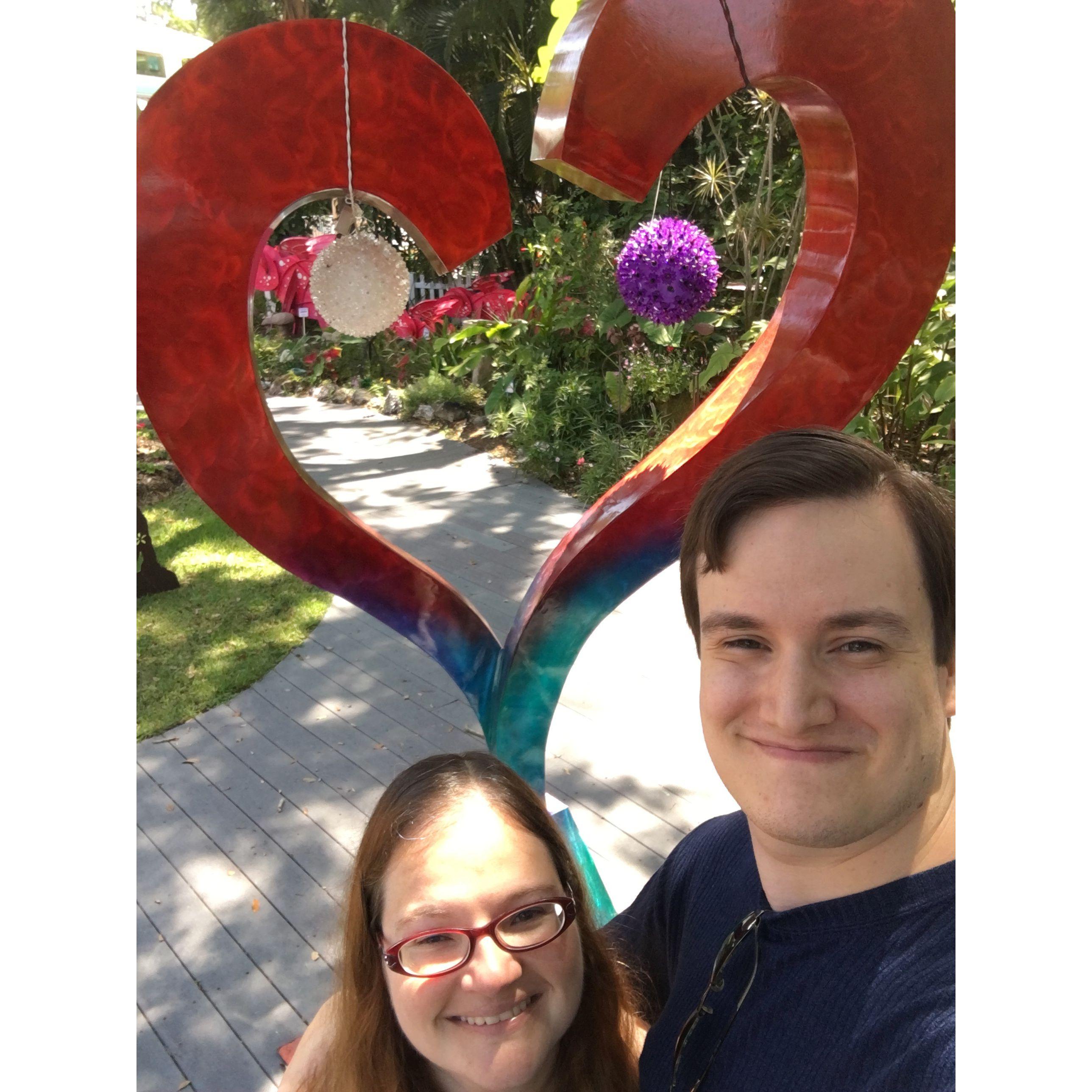 Olivia and Zac smiling in front of a heart sculpture