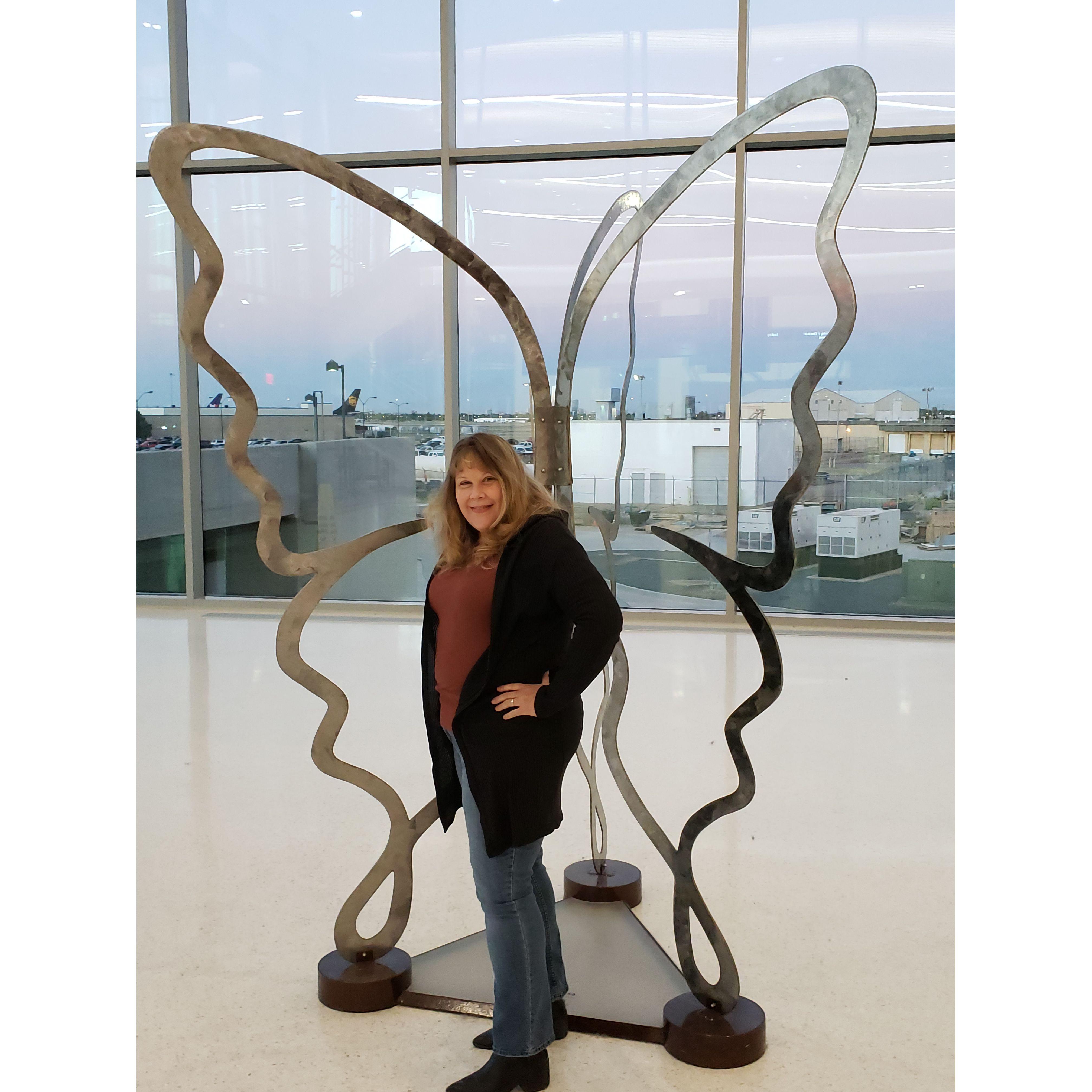 Lori at the OKC airport by a sculpture of her favorite thing, a butterfly.