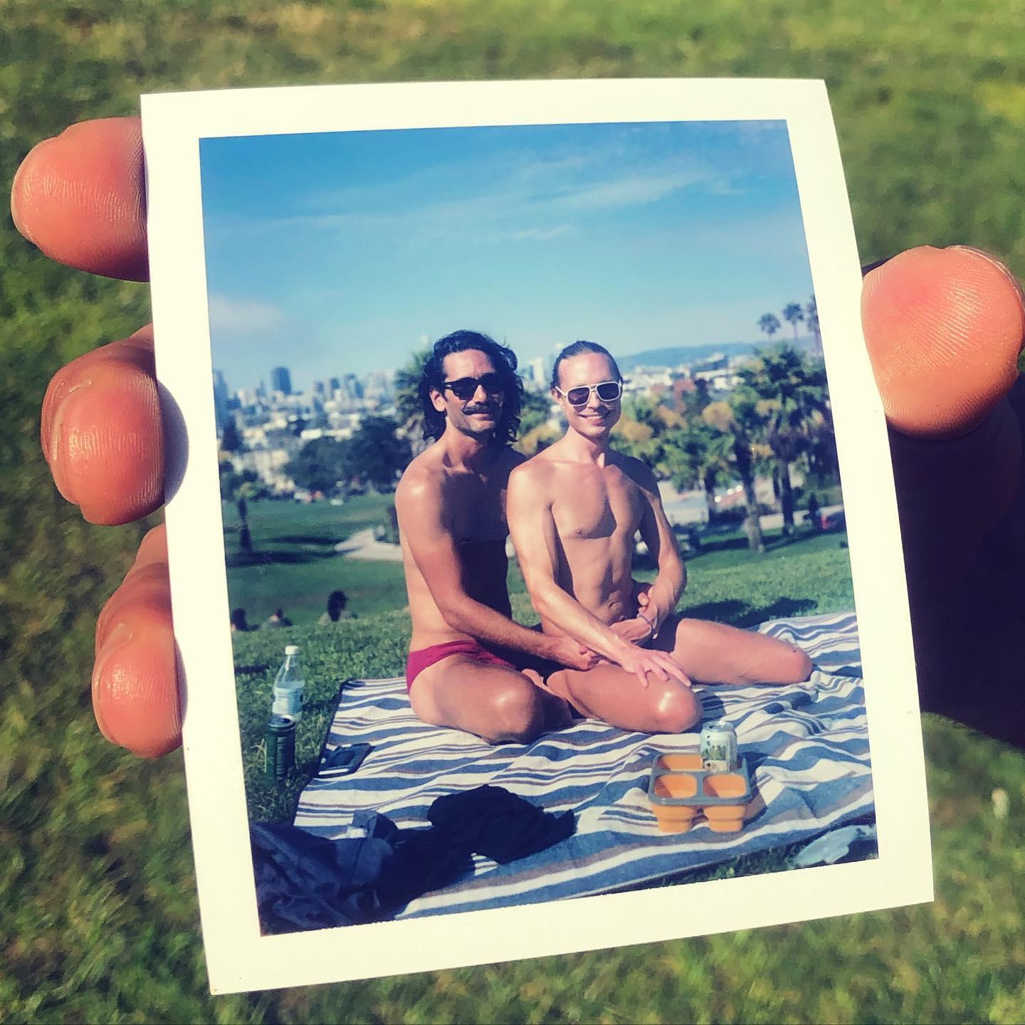 Anniversary pic. A Polaroid of us is framed by John-Paul’s hand holding the pic. We're at Delores Park, with downtown San Francisco behind us