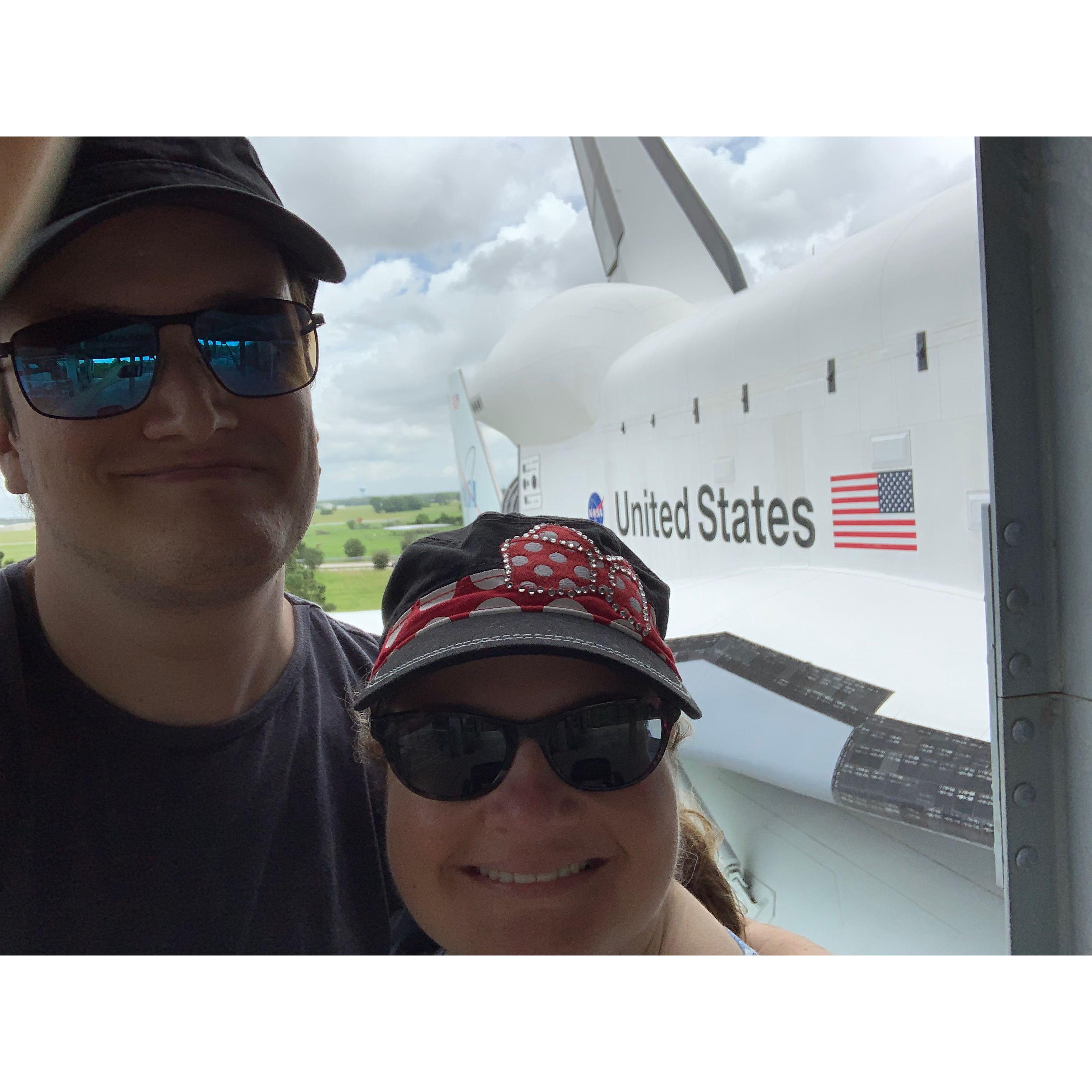 Selfie next to a NASA shuttle at the Johnson Space Center. The shuttle has the NASA logo and the American flag on it.